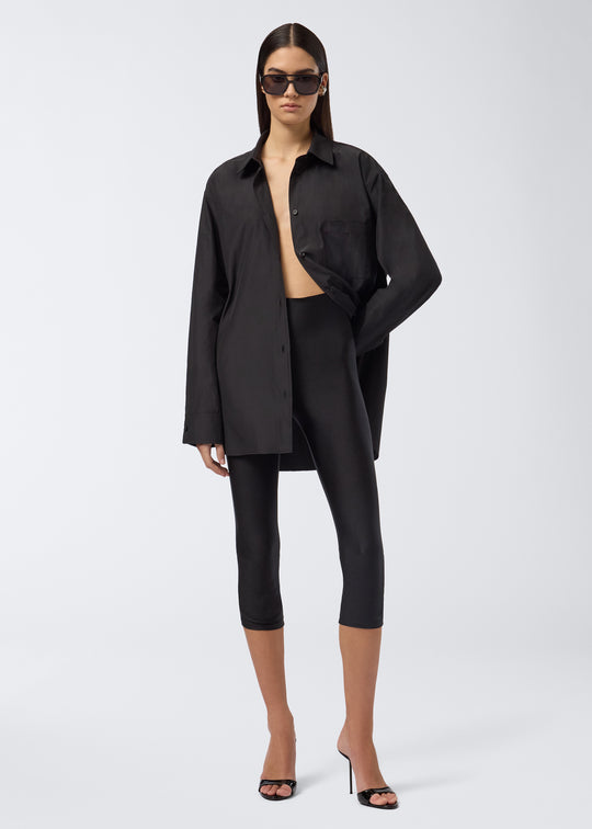 Frontal view of a model wearing Holly Capri Leggings, featuring sleek black lycra with a subtle sheen, high waist, and capri length just below the knees.