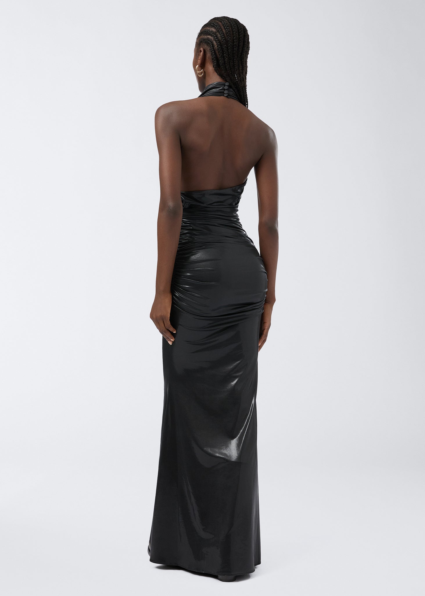 Rear view of a woman wearing the Stella Maxi Dress, a black shiny liquid jersey gown with a dramatic open back and fitted silhouette against a plain background.