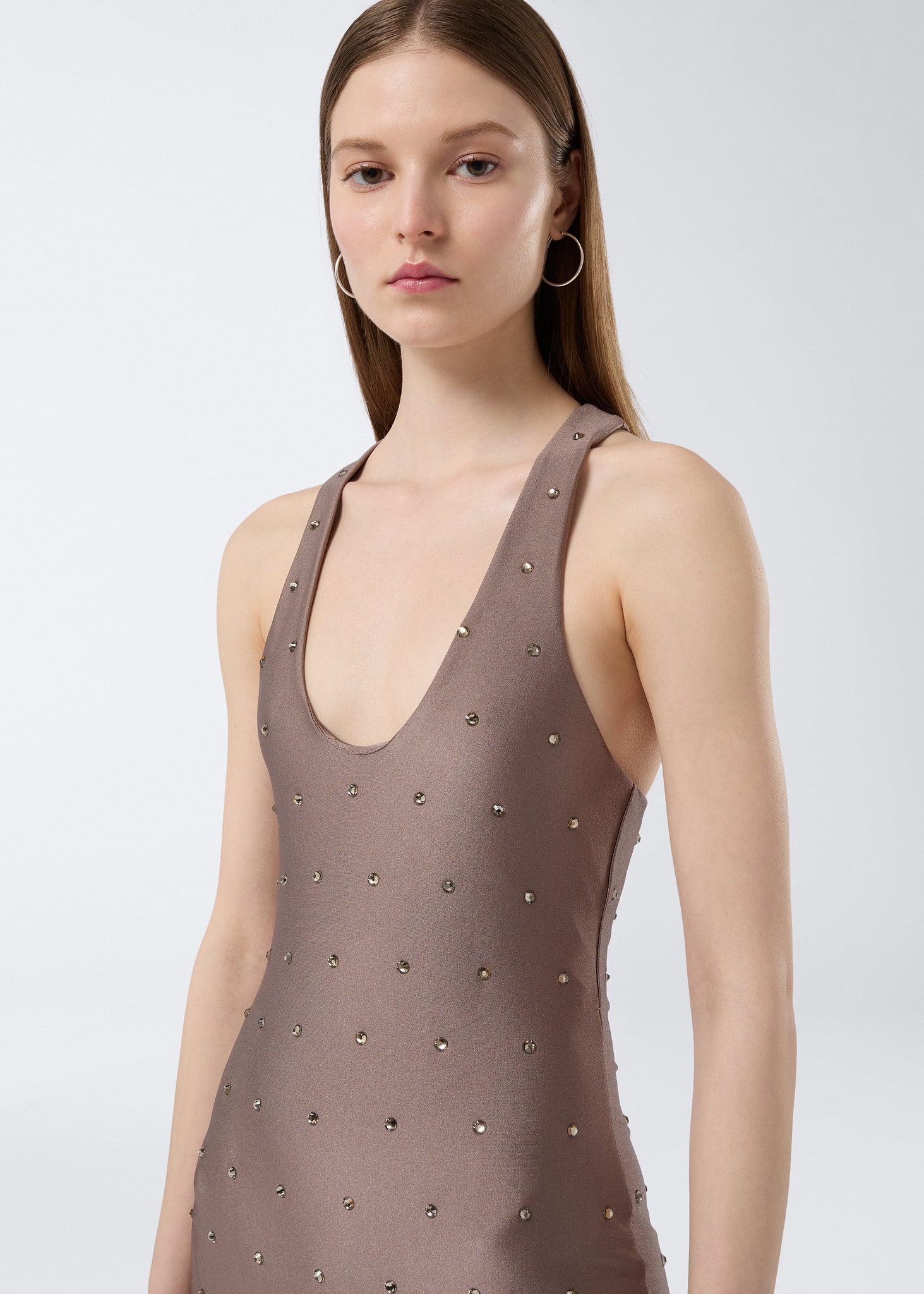 Frontal view shows a model wearing the Tess Crystal Jumpsuit in greige shiny lycra with thin straps, scoop neck, and tone-on-tone crystal embellishments.