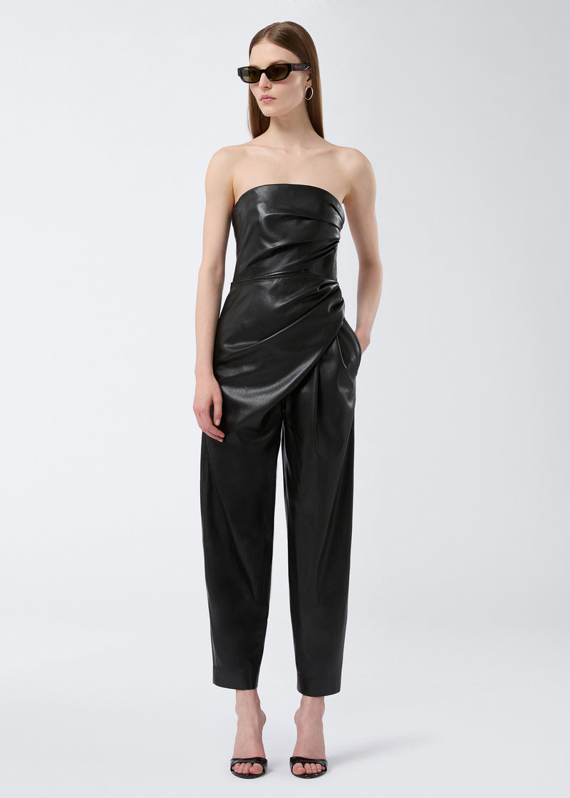 
                          Frontal view of a woman wearing the Yana Jumpsuit in black vegan leather, featuring a bustier neckline, sleeveless design, cinched waist, and draped layers.
                        