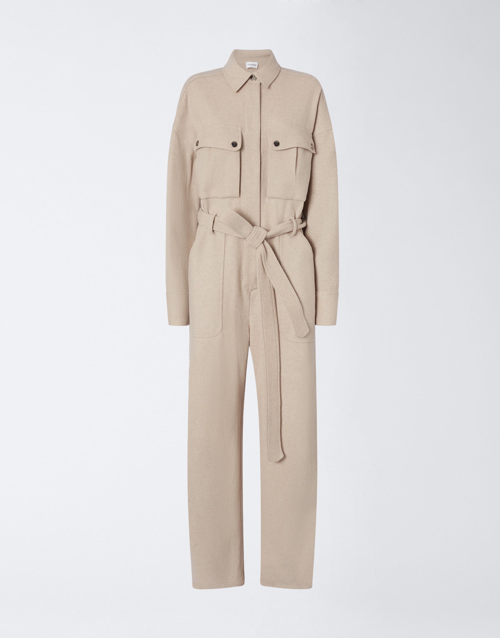 Frontal view shows the Xandra Jumpsuit in sand-colored felted jersey, with a pointed collar, concealed button placket, long sleeves, patch pockets, and a matching belt.