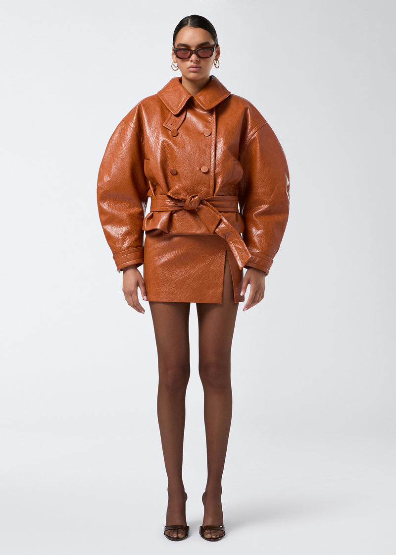 
                          Frontal view of a model wearing the Gioia Mini Skirt in cuoio embossed eco leather, featuring a high waist, thigh slit, and side zip closure.
                        