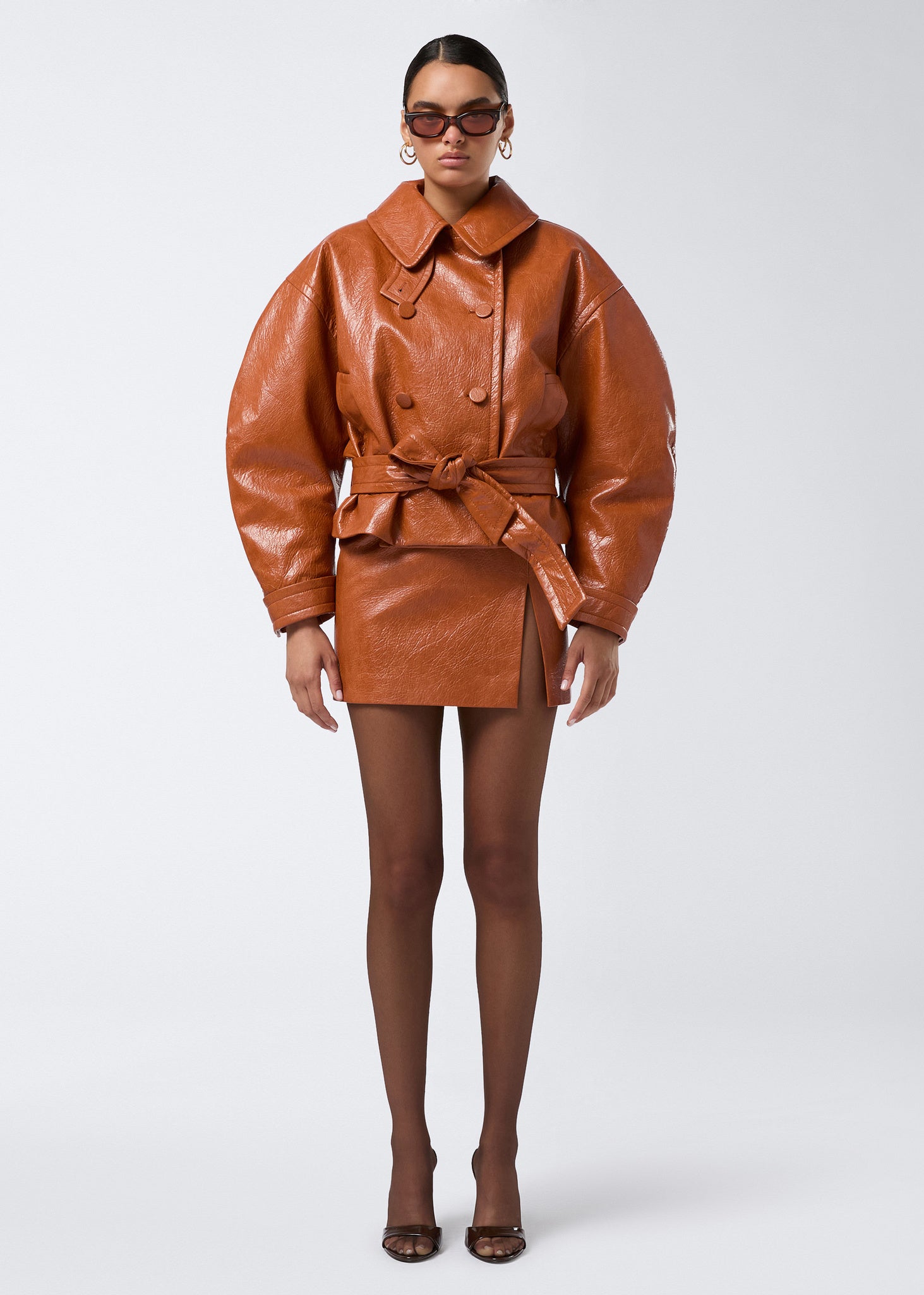 Frontal view of a model wearing the Gioia Mini Skirt in cuoio embossed eco leather, featuring a high waist, thigh slit, and side zip closure.