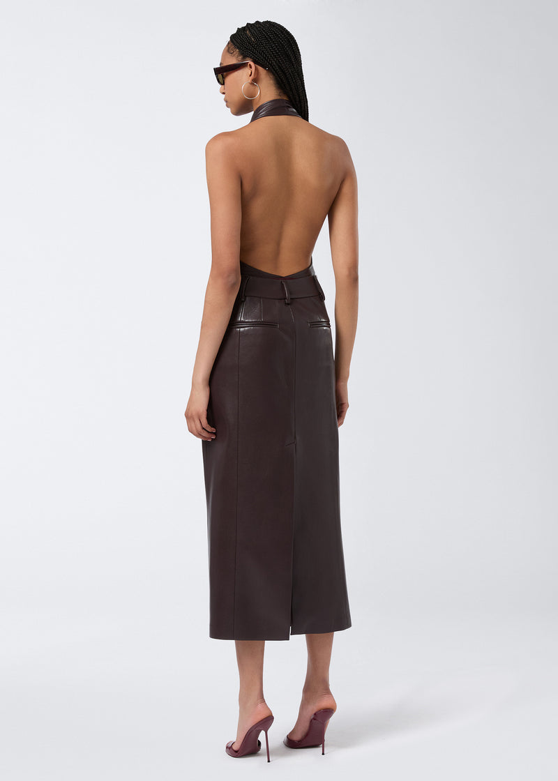
                          Rear view of model wearing Xania Midi Skirt in cabernet vegan leather, showing back slit, belt loops, and two back pockets against a plain background.
                        