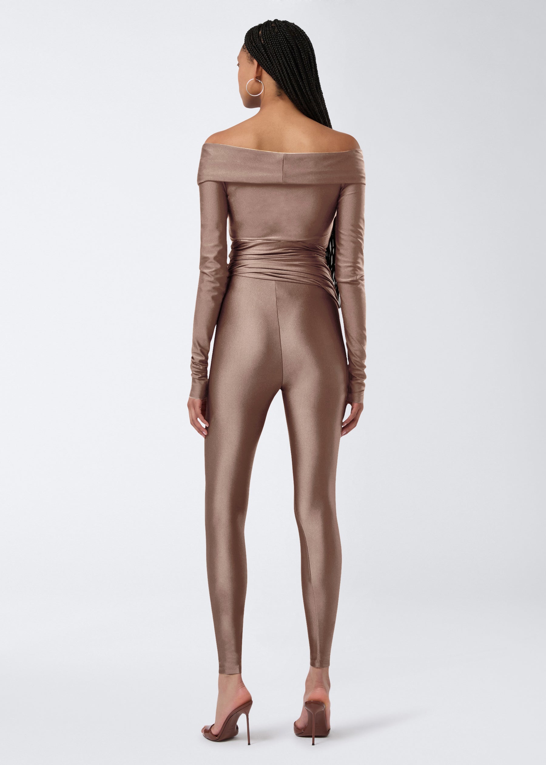 Rear view of a model wearing Vicky Leggings in a greige shiny lycra, featuring high waist, full-length fit, and draped fabric around the waist.