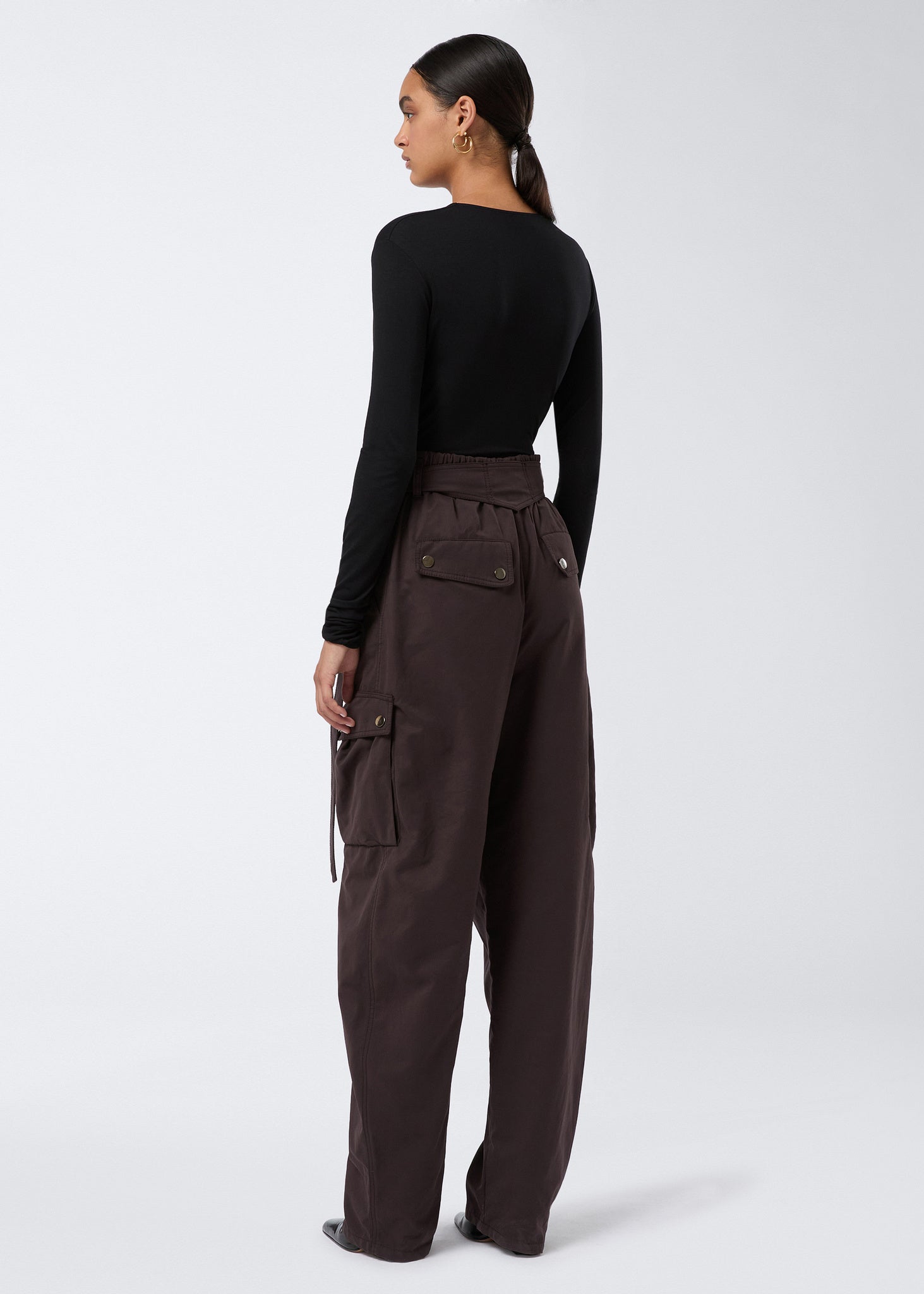 Rear view shows model wearing Xandra Maxi Pants in dark brown suede-touch nylon with buttoned thigh and back pockets, elasticated waist, and relaxed fit.