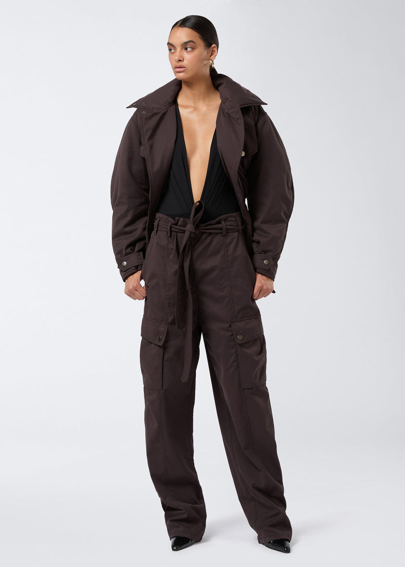 
                          Frontal view of a model wearing the Xandra Maxi Pants in dark brown, featuring a relaxed silhouette with button thigh and back pockets, an elasticated waist with adjustable belt, and zip/button front closure.
                        