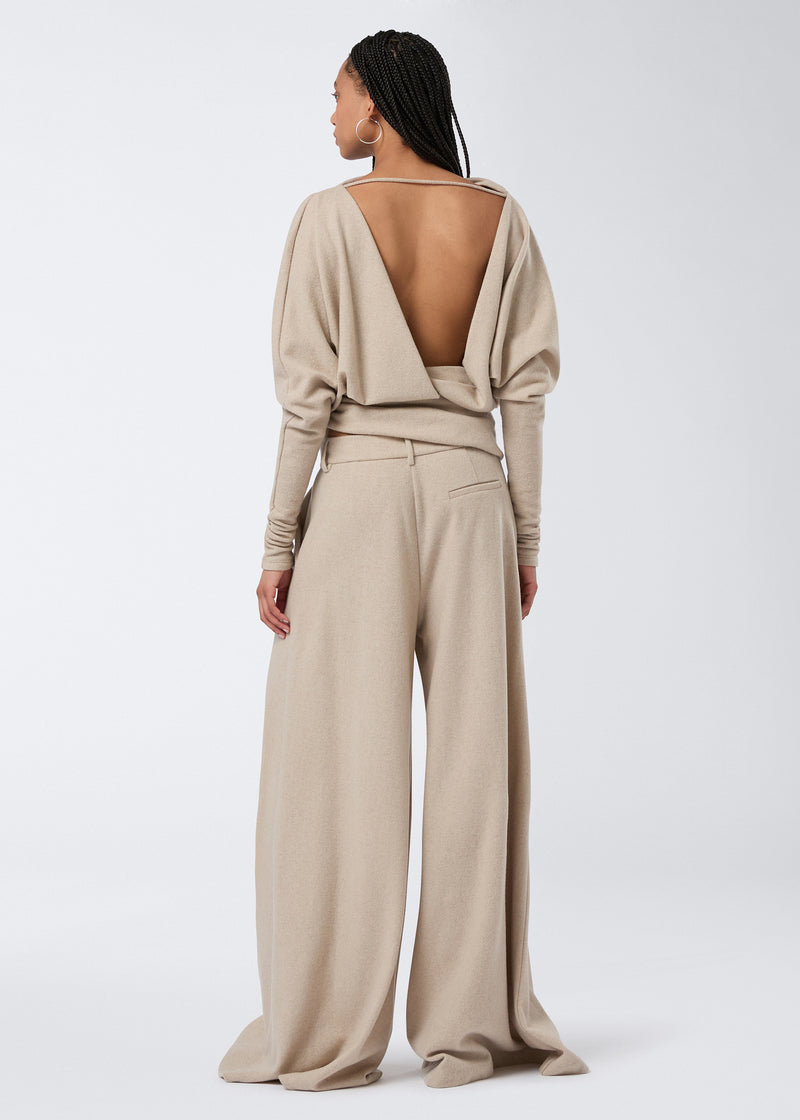 
                          Rear view of a woman wearing Tara Maxi Pants in sand-colored soft felted jersey with a super oversized, wide-leg silhouette, belt loops, and back pocket.
                        
