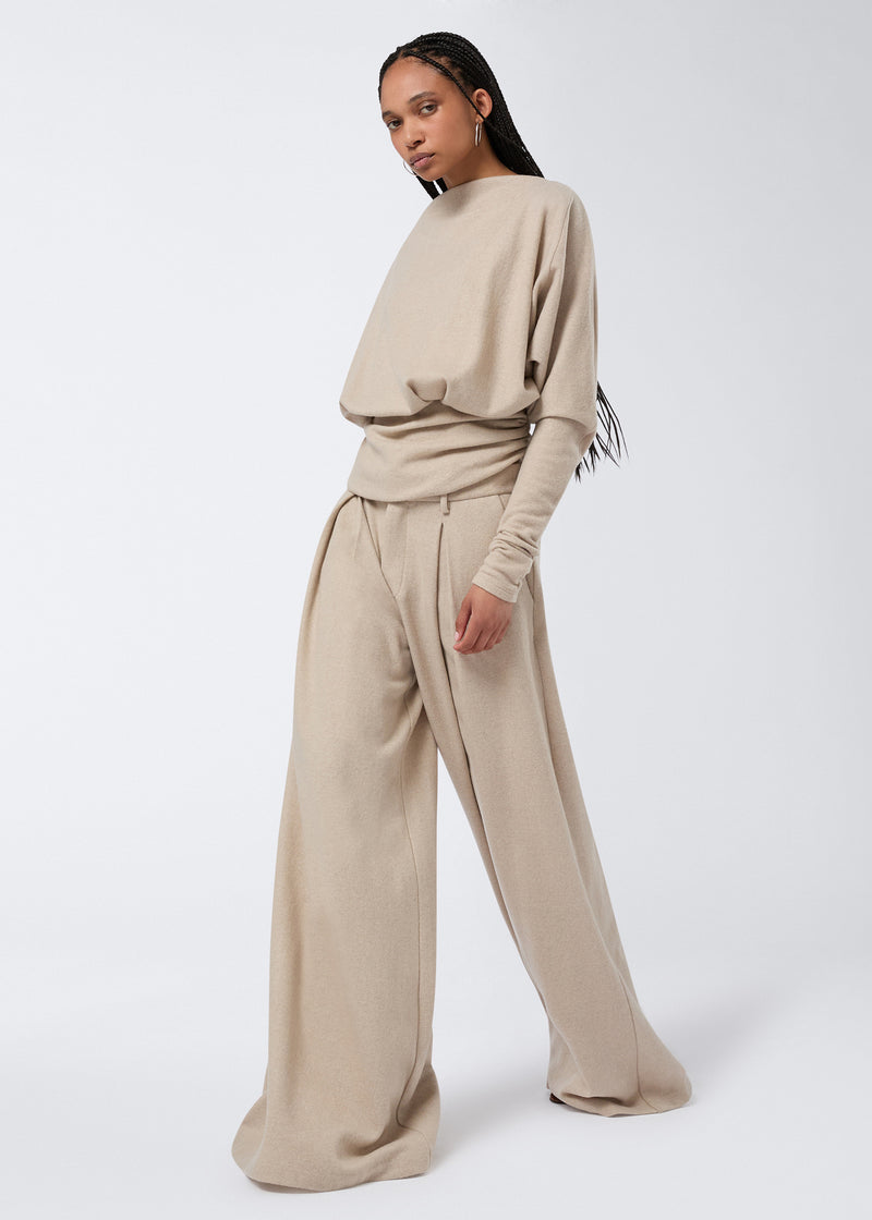 
                          Frontal view of a model wearing Tara Maxi Pants in sand-colored soft felted jersey, featuring an oversized, wide-leg silhouette with pleats and side pockets.
                        