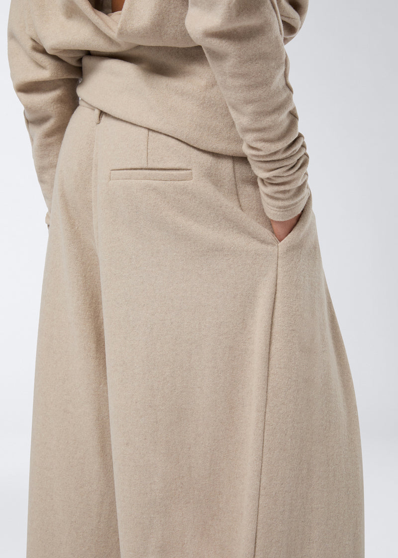 
                          Side view shows a model wearing Tara Maxi Pants in sand-colored soft felted jersey, with one hand in the side pocket and visible back pocket detail.
                        