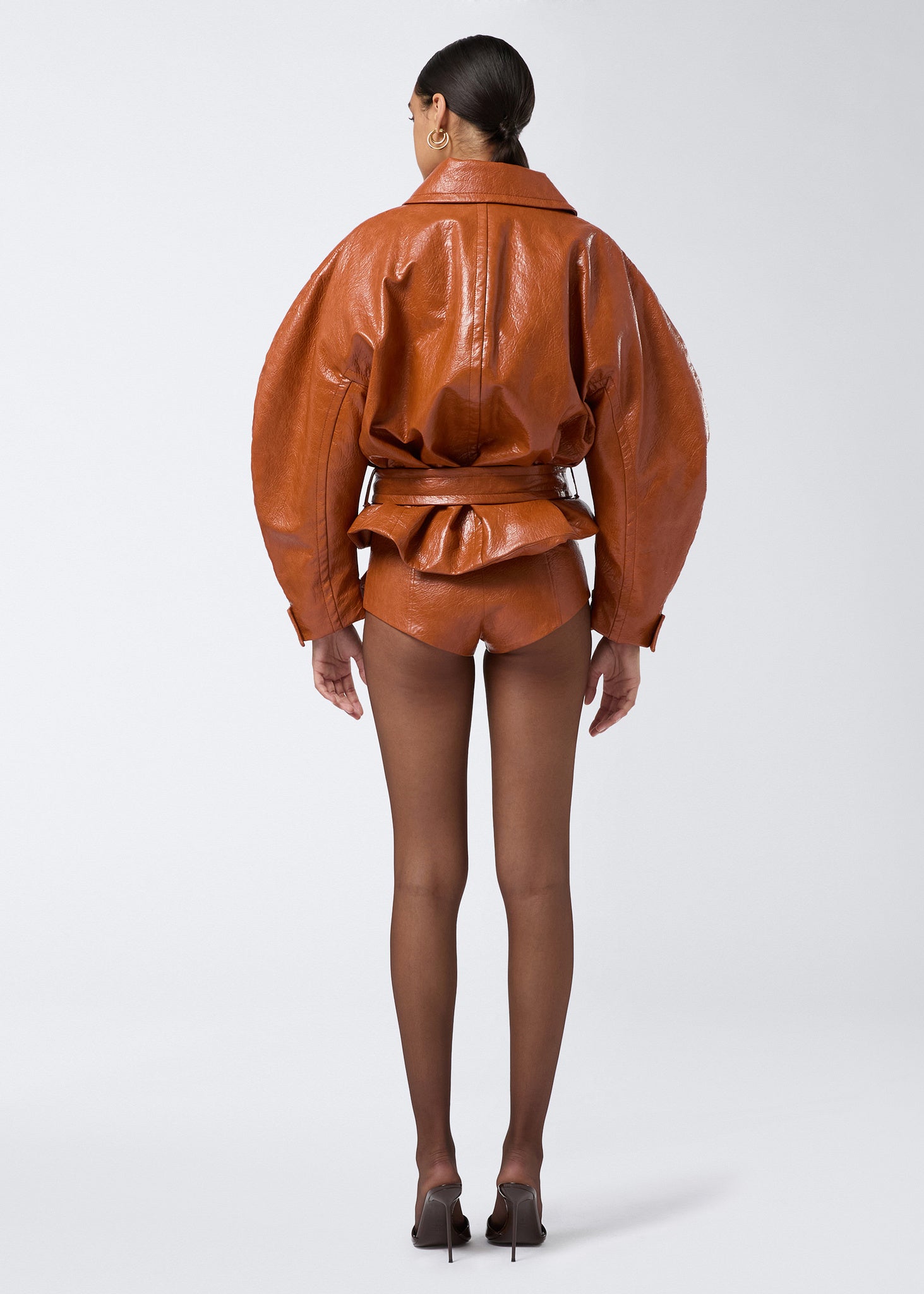 Rear view of a model wearing Tami Culottes in cuoio embossed eco-leather, featuring a high-waist, side zip fastening, paired with matching oversized jacket.
