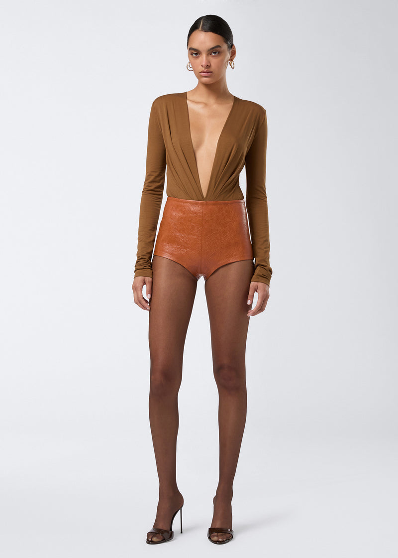 
                          Frontal view of a model wearing Tami Culottes in cuoio embossed eco-leather, featuring a high waist and structured fit paired with sheer tights and heels.
                        