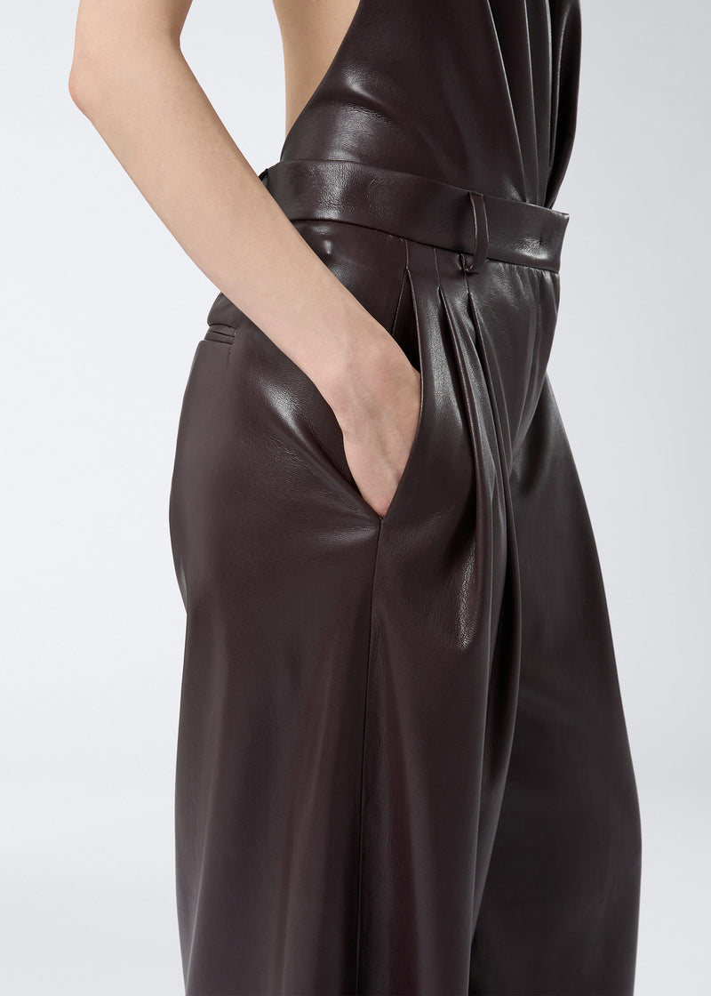 
                          Side view shows a model wearing Tracy Maxi Pants in cabernet-colored vegan leather with pleats, side slit pocket, and belt loops at the waist.
                        