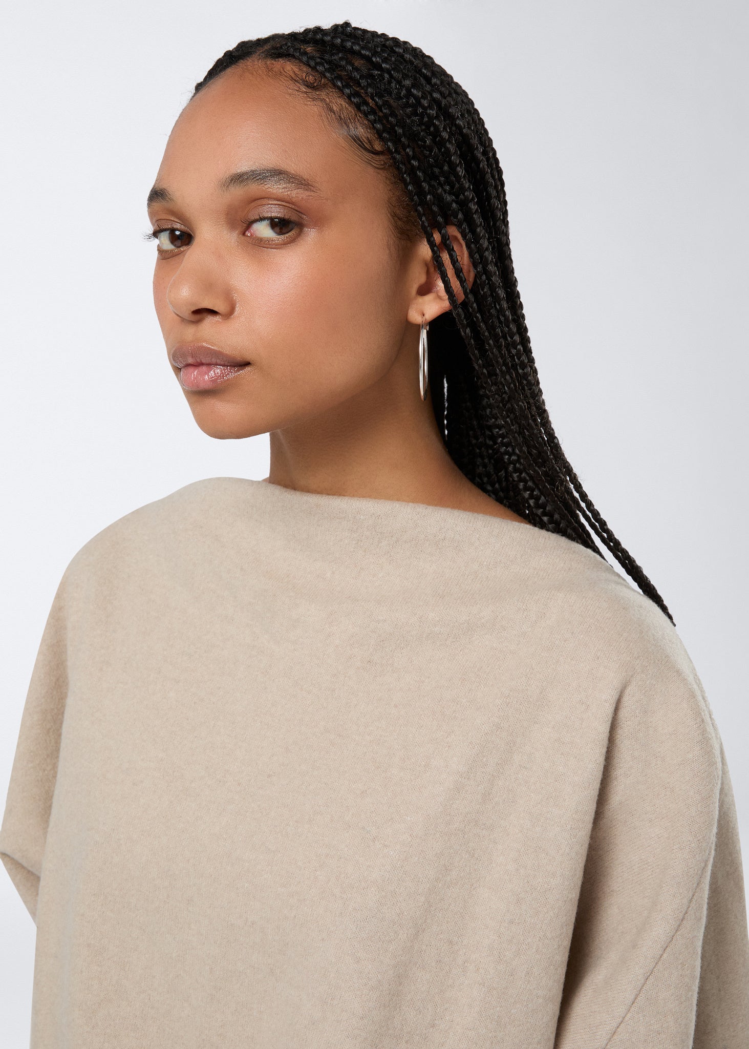 Frontal view showing a model wearing the Wisteria Top in sand-colored soft felted jersey, featuring a high boat neckline and long sleeves.