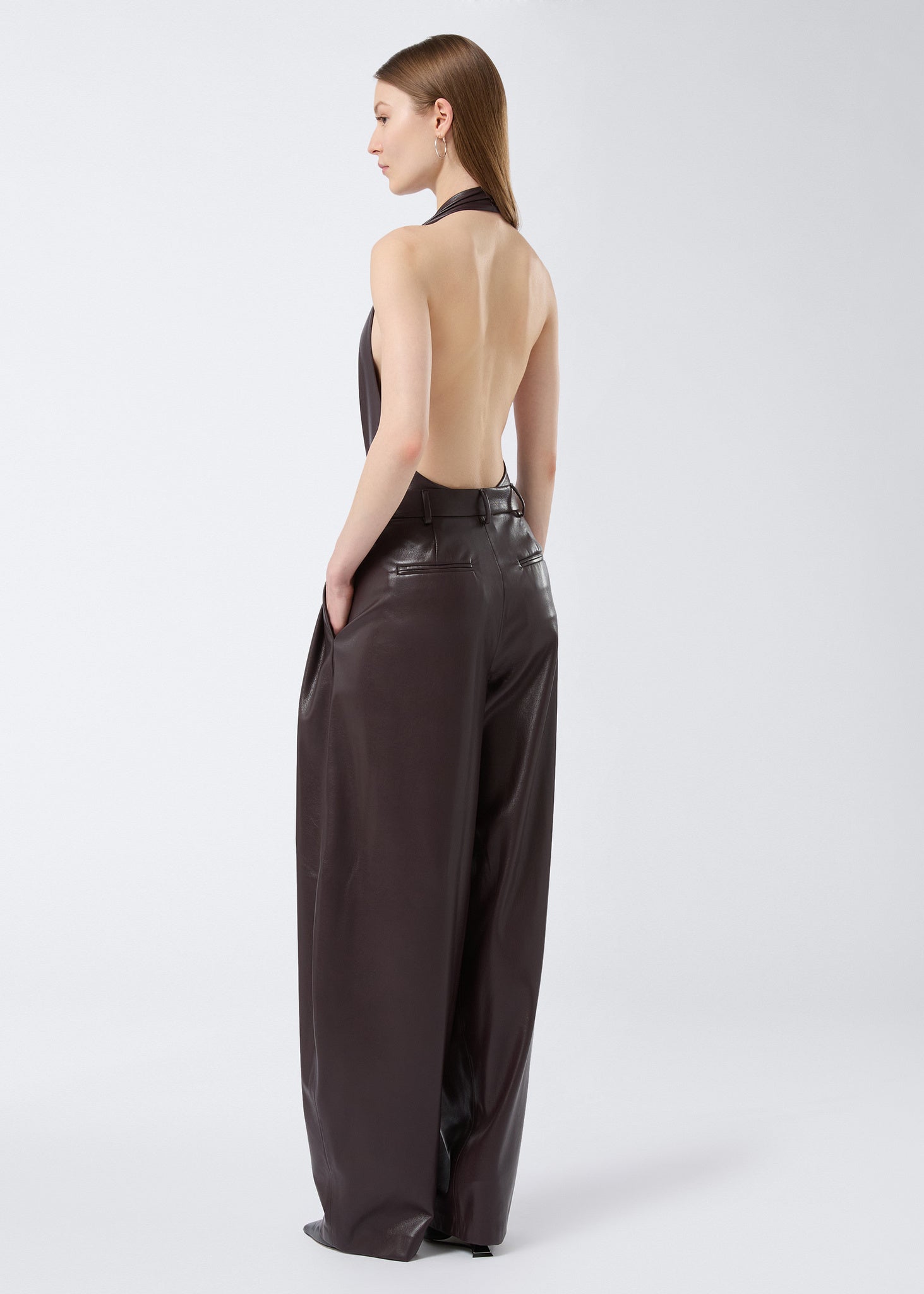 Rear view of a woman wearing the Zendaya Bodysuit in cabernet vegan leather, featuring a halterneck strap, backless design, and sleeveless cut.