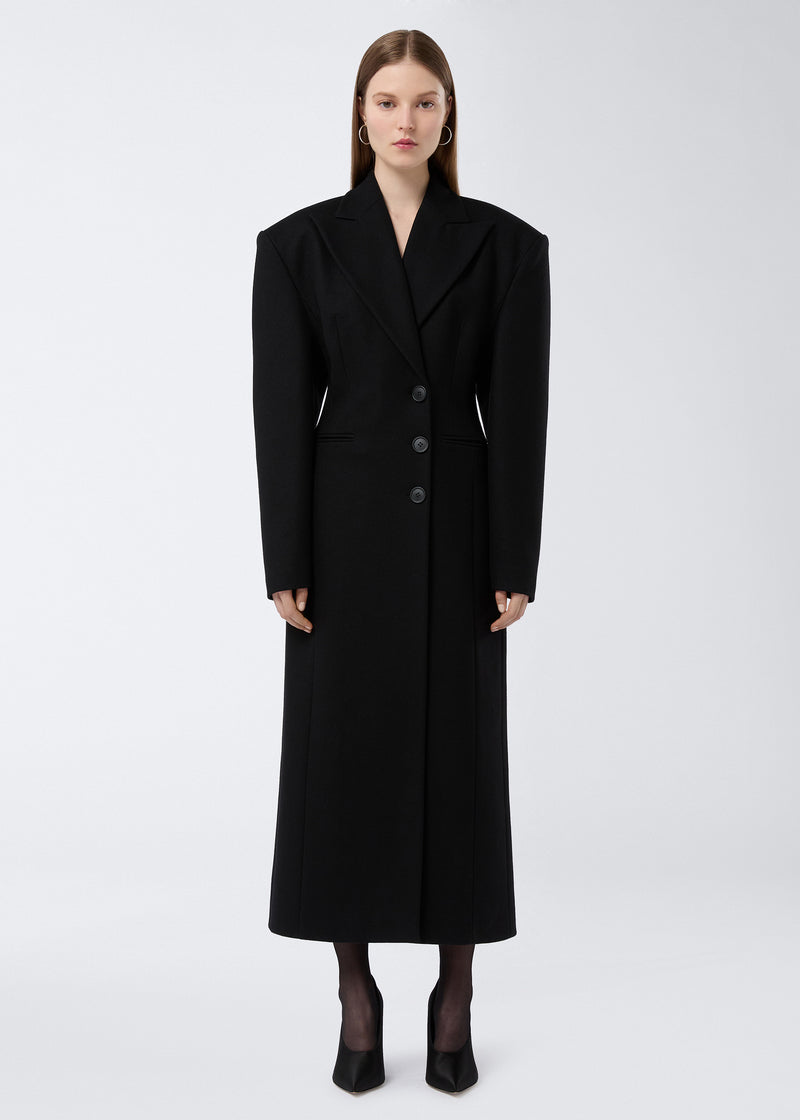 
                          Frontal view of Ottavia Coat, a long black felted wool women’s coat with exaggerated padded shoulders, pointed lapel collar, three front buttons, and defined waist.
                        