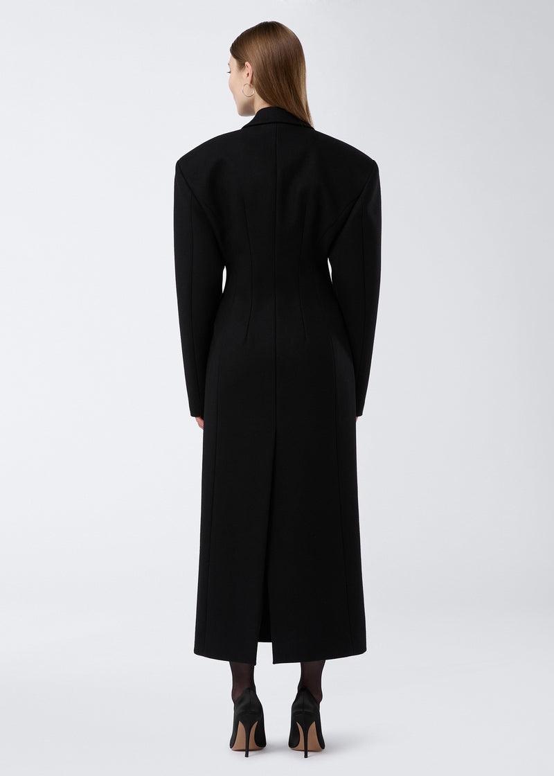 
                          Rear view of a woman wearing the Ottavia Coat in black felted wool, displaying its hourglass silhouette, padded shoulders, and back vent detail.
                        