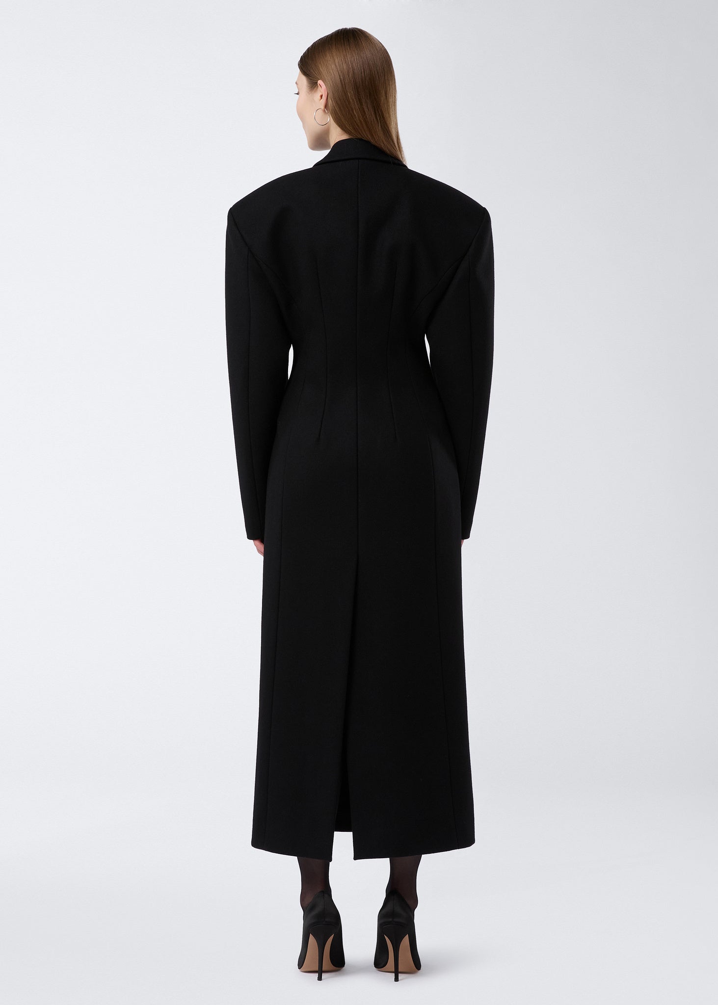 Rear view of a woman wearing the Ottavia Coat in black felted wool, displaying its hourglass silhouette, padded shoulders, and back vent detail.