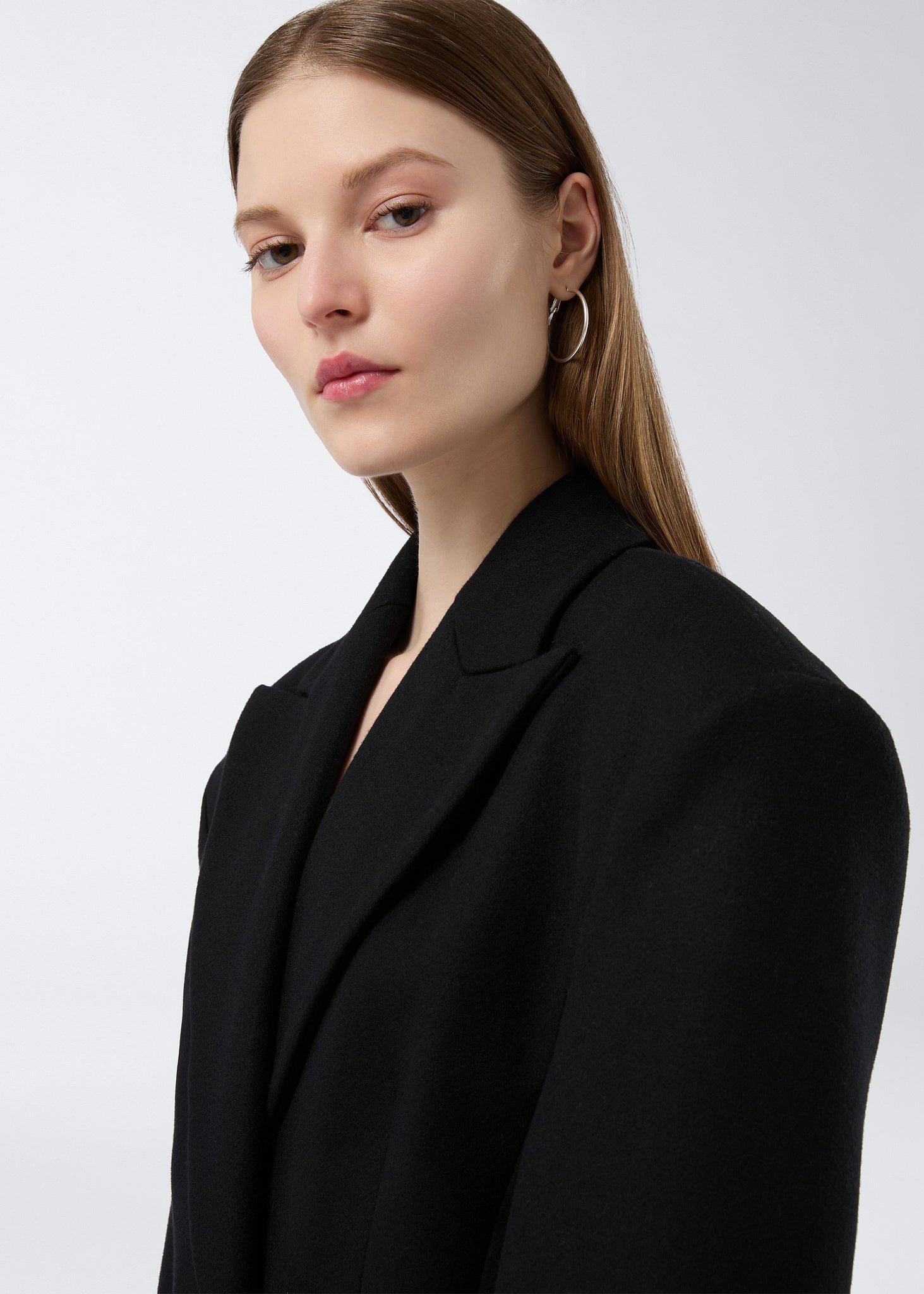 Frontal detail view of a woman wearing the Ottavia Coat in black felted wool, highlighting the padded shoulders, well-defined waist, and pointed lapel collar.