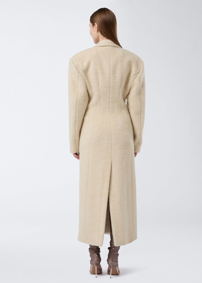 
                          Rear view: Model stands wearing the Ottavia Coat in ivory soft wool twill, showing off padded shoulders, defined waist, and a back vent detail.
                        