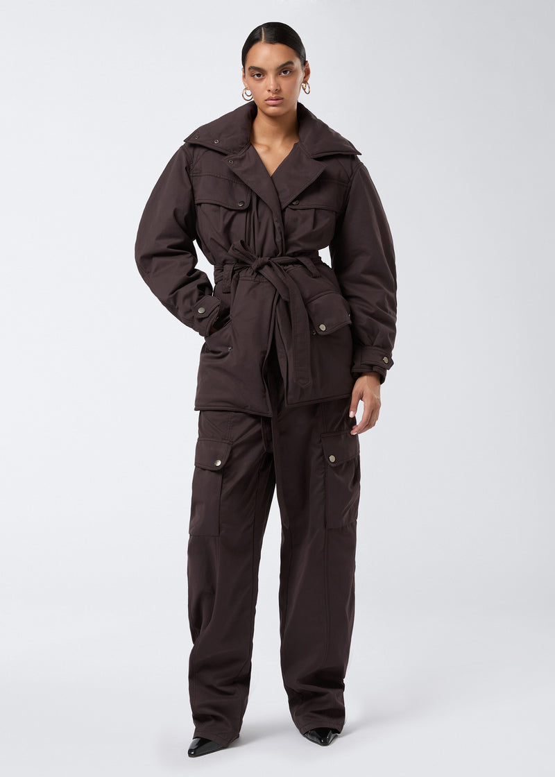 
                          Frontal view of a woman wearing the Xandra Jacket in dark brown suede-touch nylon, featuring an oversized spread collar, four flap pockets, a matching belt, and buttoned cuffs.
                        