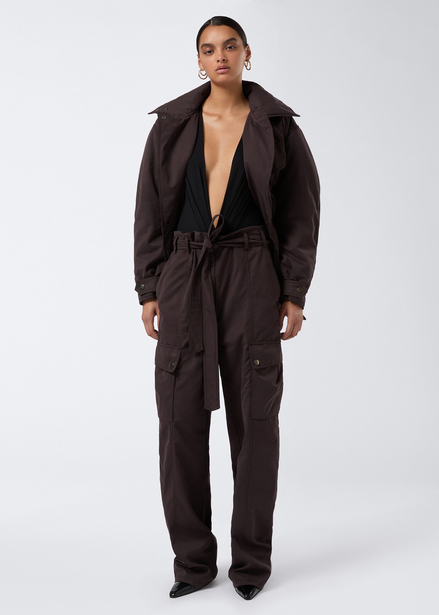 Frontal view of a woman wearing the Xandra Jacket in dark brown structured suede-touch nylon, featuring an oversized collar, belt, and four flap pockets.