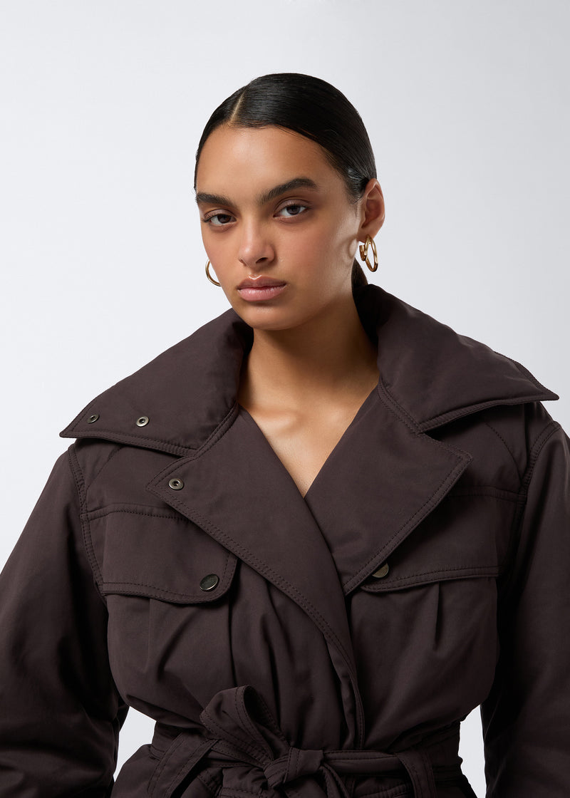 
                          Frontal view of a woman wearing the Xandra Jacket in dark brown suede-touch nylon, featuring an oversized collar, flap pockets, and a matching belt tied at the waist.
                        