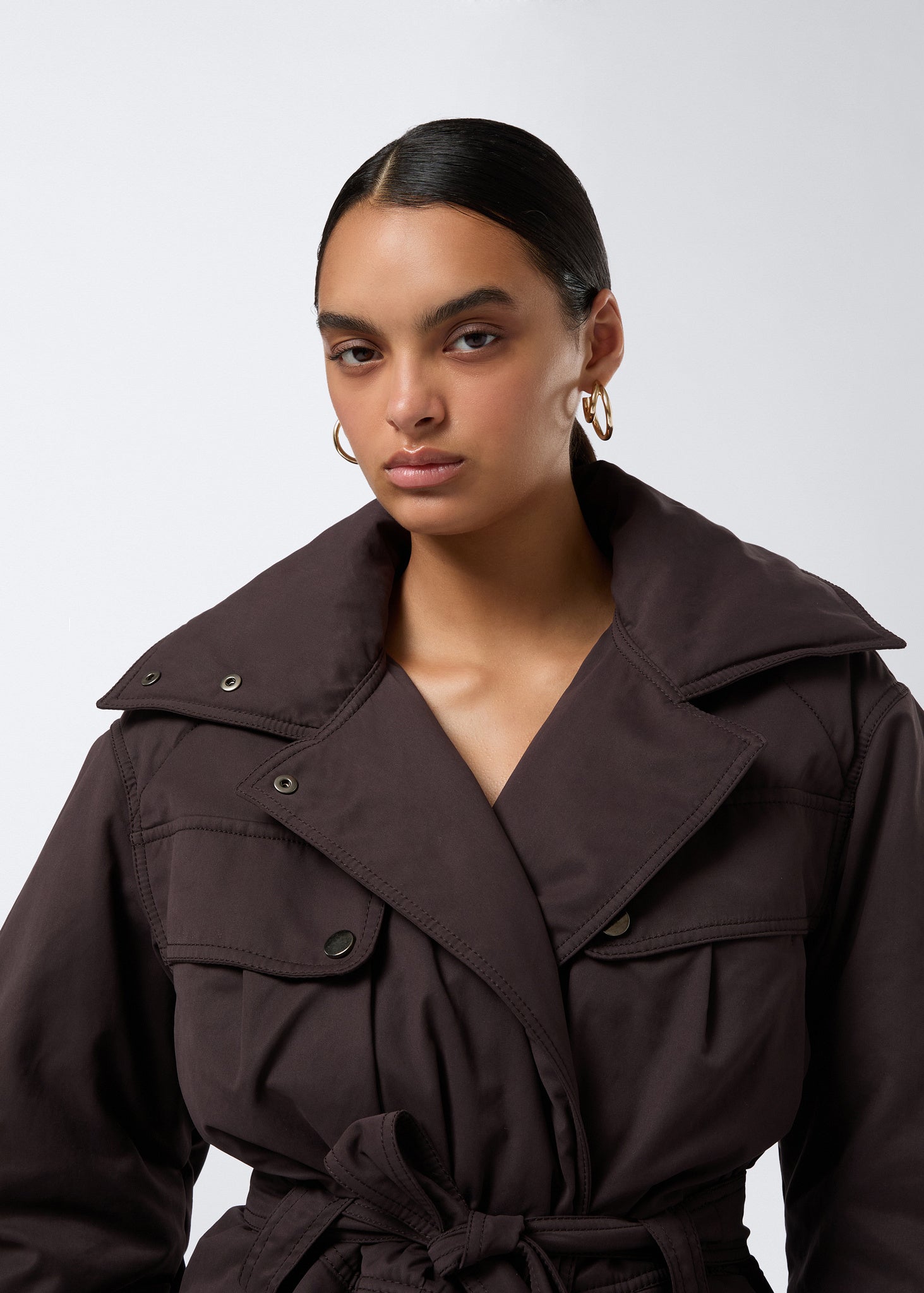 Frontal view of a woman wearing the Xandra Jacket in dark brown suede-touch nylon, featuring an oversized collar, flap pockets, and a matching belt tied at the waist.