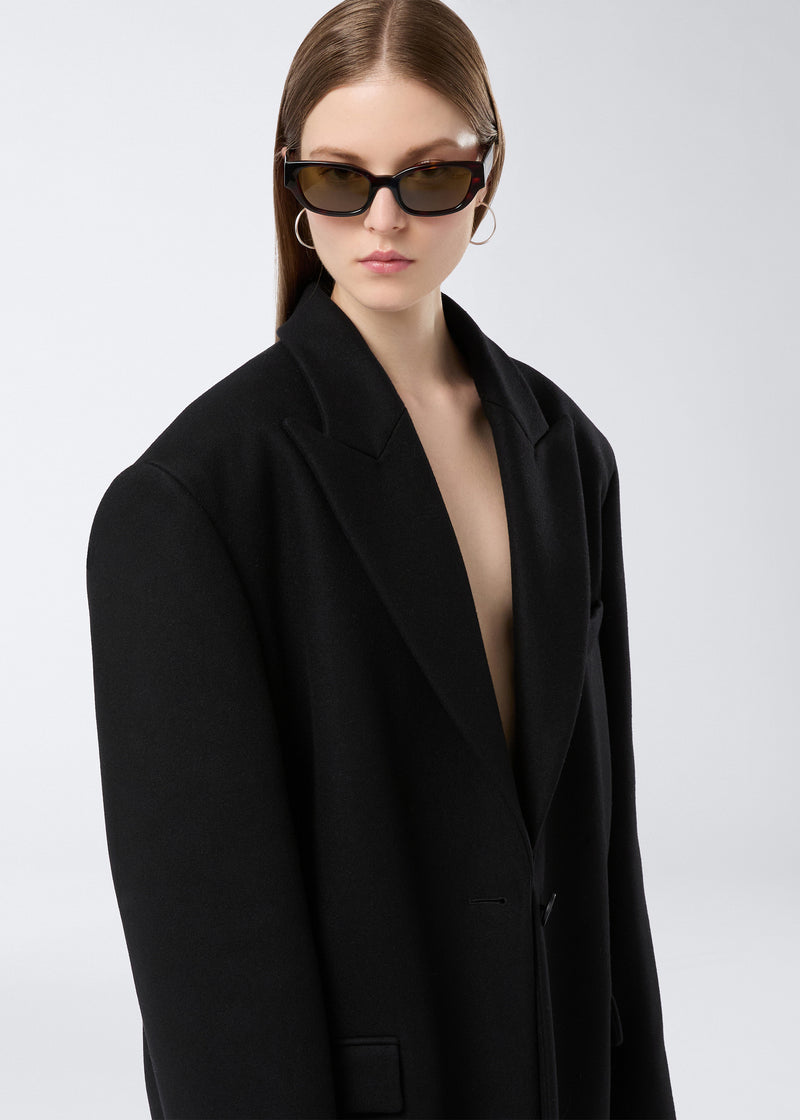
                          Frontal view: A model wears the Teresa Blazer, an oversized black felted wool blazer with peaked lapels and single-breasted closure, styled elegantly.
                        