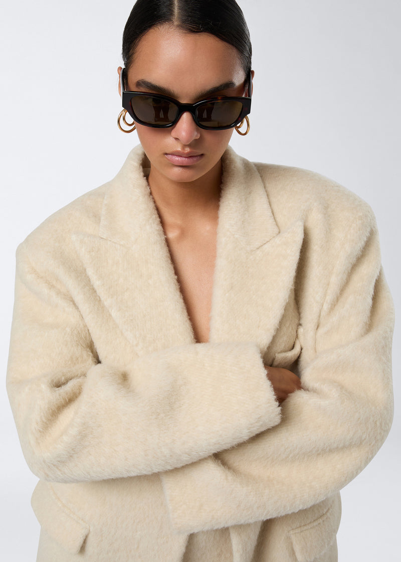 
                          Frontal view shows a model wearing the Teresa Blazer in ivory soft wool twill, featuring a fluffy oversized design with peaked lapel and padded shoulders.
                        
