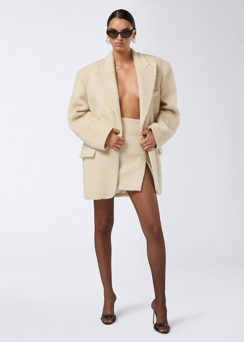 
                          Frontal view of a woman wearing the Teresa Blazer, an oversized ivory soft wool twill blazer with a fluffy finish, peaked lapel, single button closure, and flap pockets.
                        