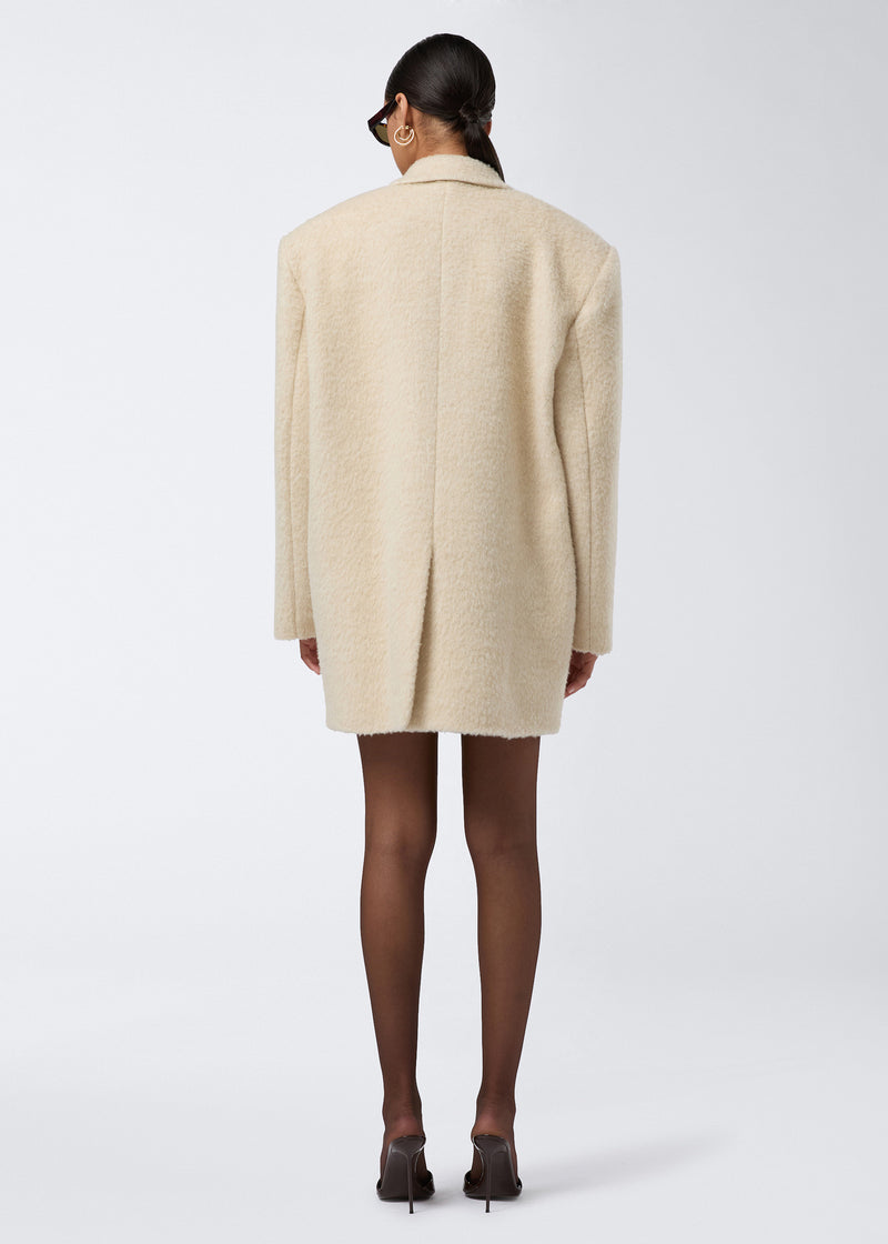 
                          Rear view of a woman wearing the Teresa Blazer in ivory soft wool twill, featuring an oversized fit, fluffy finish, and a back vent.
                        