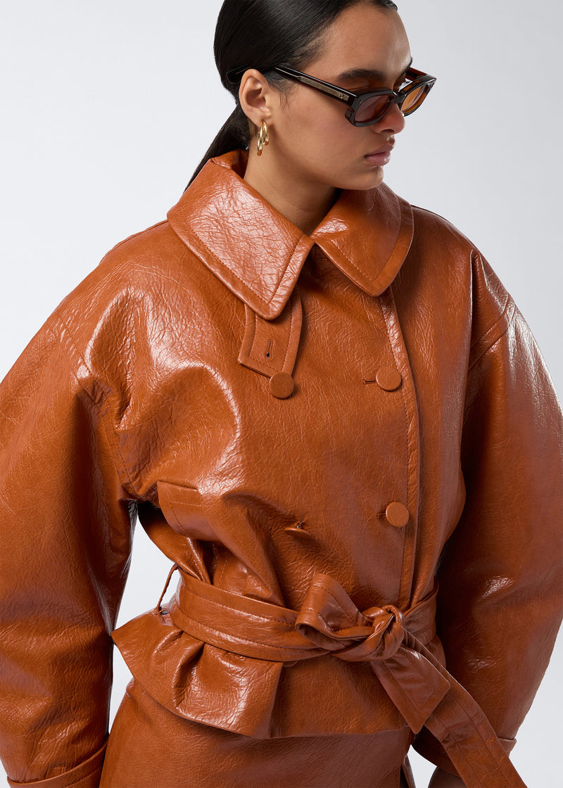 
                          Frontal view of Zarina Coat in a cuoio shade of embossed eco leather, showing large collar, notched lapel, double-breasted closure, and matching belt.
                        