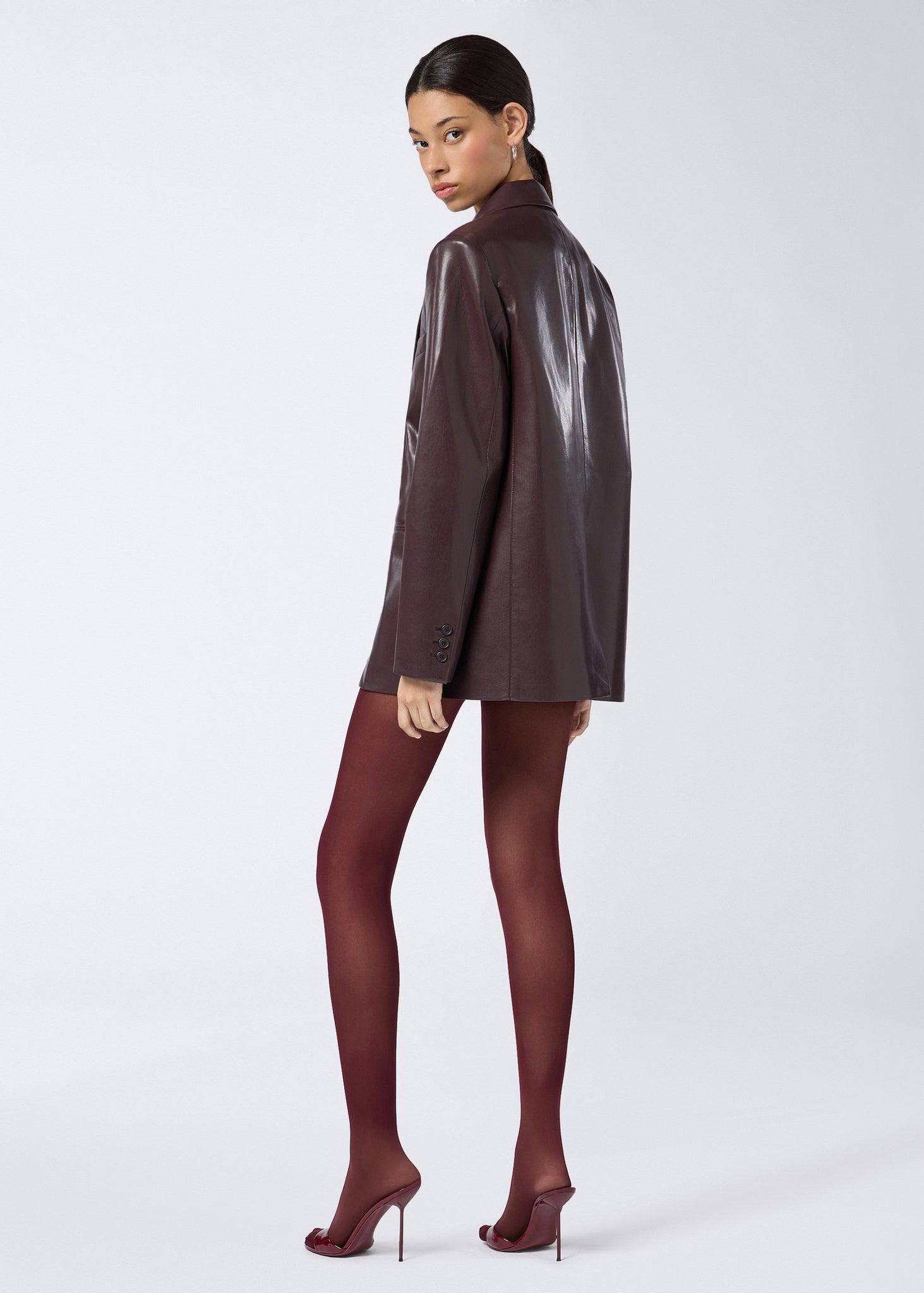 Rear view showing a model wearing the Guia Blazer in cabernet vegan leather, featuring an oversized fit, notched lapel, and buttoned cuffs.