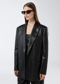 Frontal view of a woman wearing the Guia Blazer in black vegan leather, showing its oversized fit, notched lapel, chest welt pocket, and single-breasted closure.