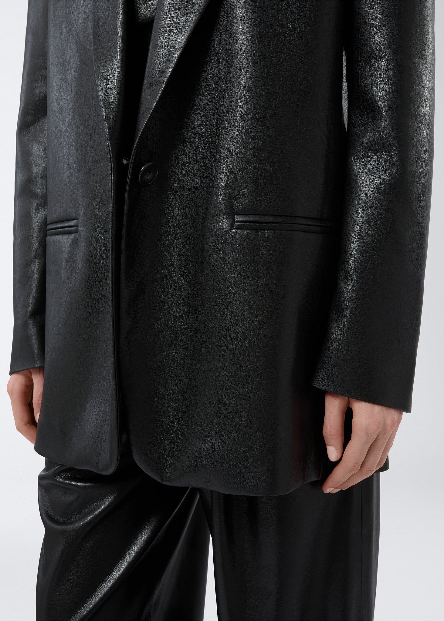 Frontal view showing a person wearing the Guia Blazer in black vegan leather, highlighting the ultra-soft texture, single-breasted closure, and welt pockets.