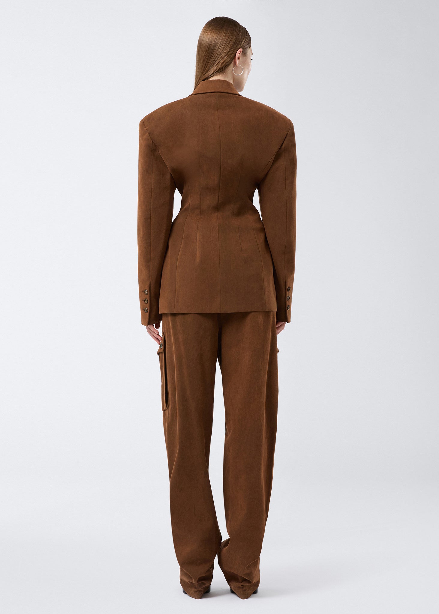Rear view shows a model wearing the Ottavia Blazer in cigar-colored, stone-washed cotton, featuring a belted hourglass shape and structured shoulders.