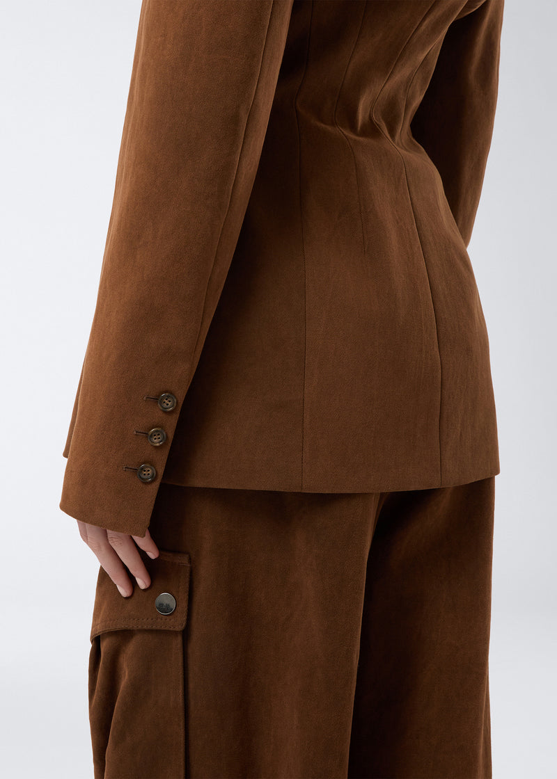 
                          Detail view shows the Ottavia Blazer in cigar-colored, stone-washed cotton, highlighting three buttoned cuffs, a cinched waist, and part of the matching pants.
                        