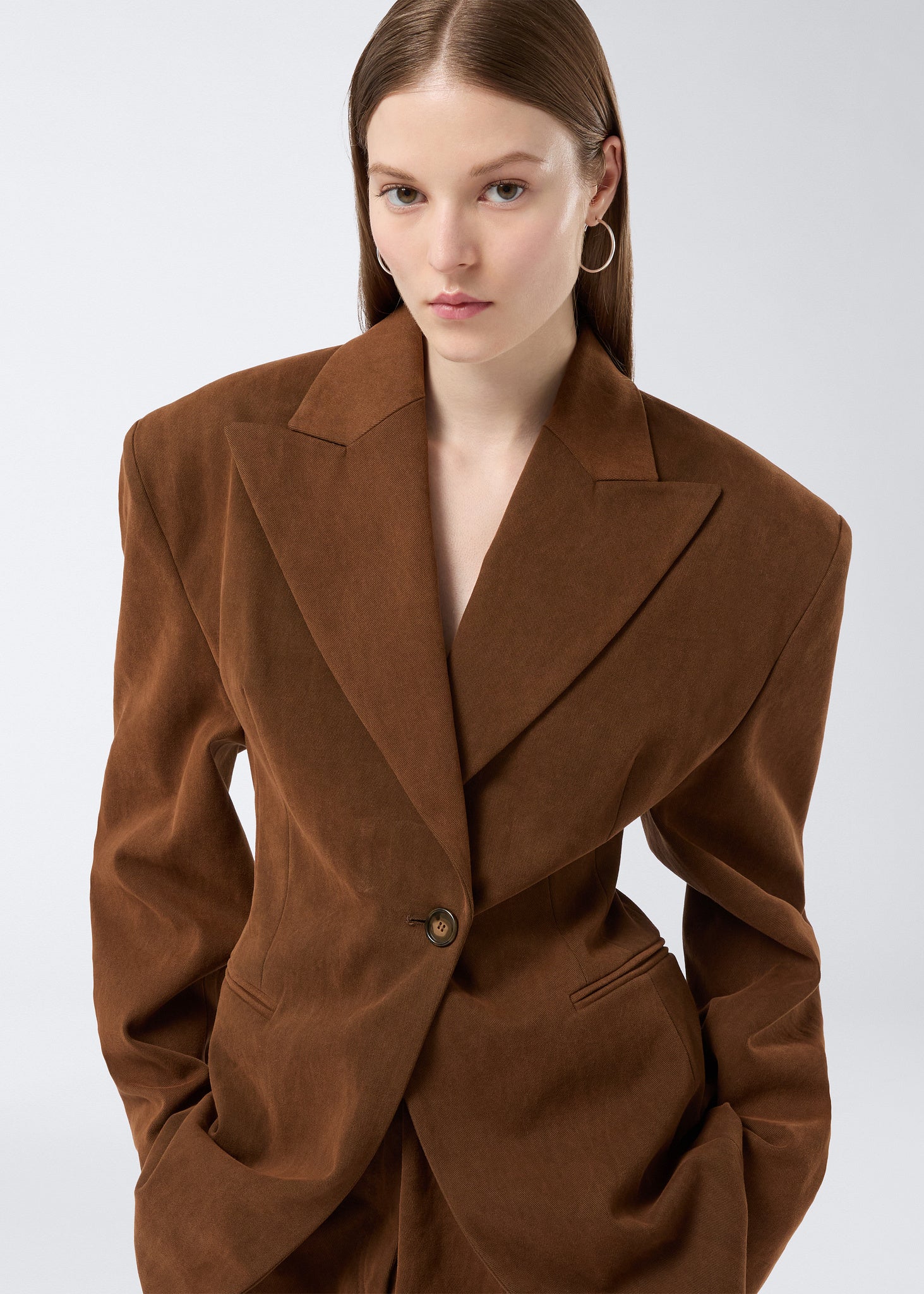 Frontal view of a model wearing the Ottavia Blazer, a cigar-colored, stone-washed cotton blazer with peaked lapel, cinched waist, and padded shoulders.