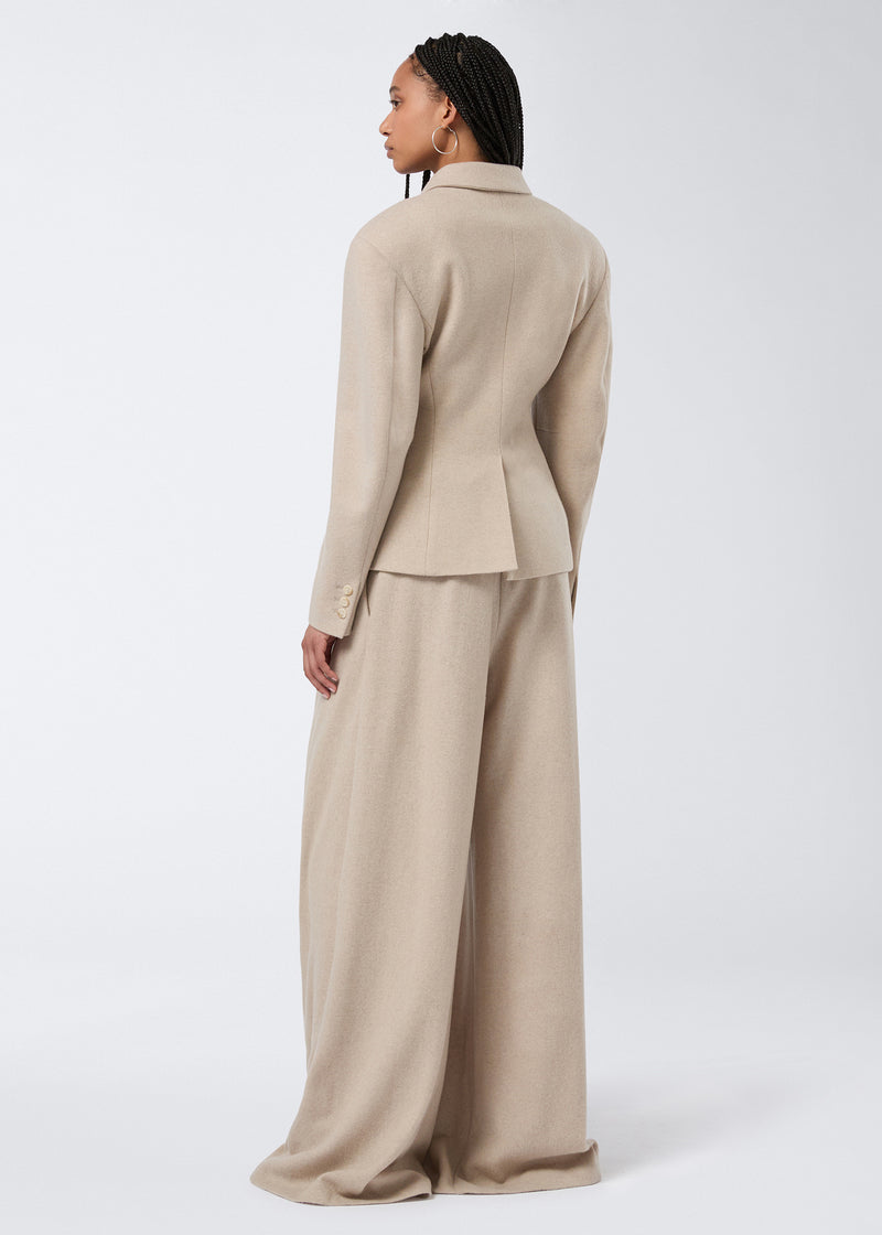 
                          Rear view shows a model wearing the Tillie Blazer in sand-colored soft felted jersey, featuring a back vent, buttoned cuffs, and padded shoulders.
                        