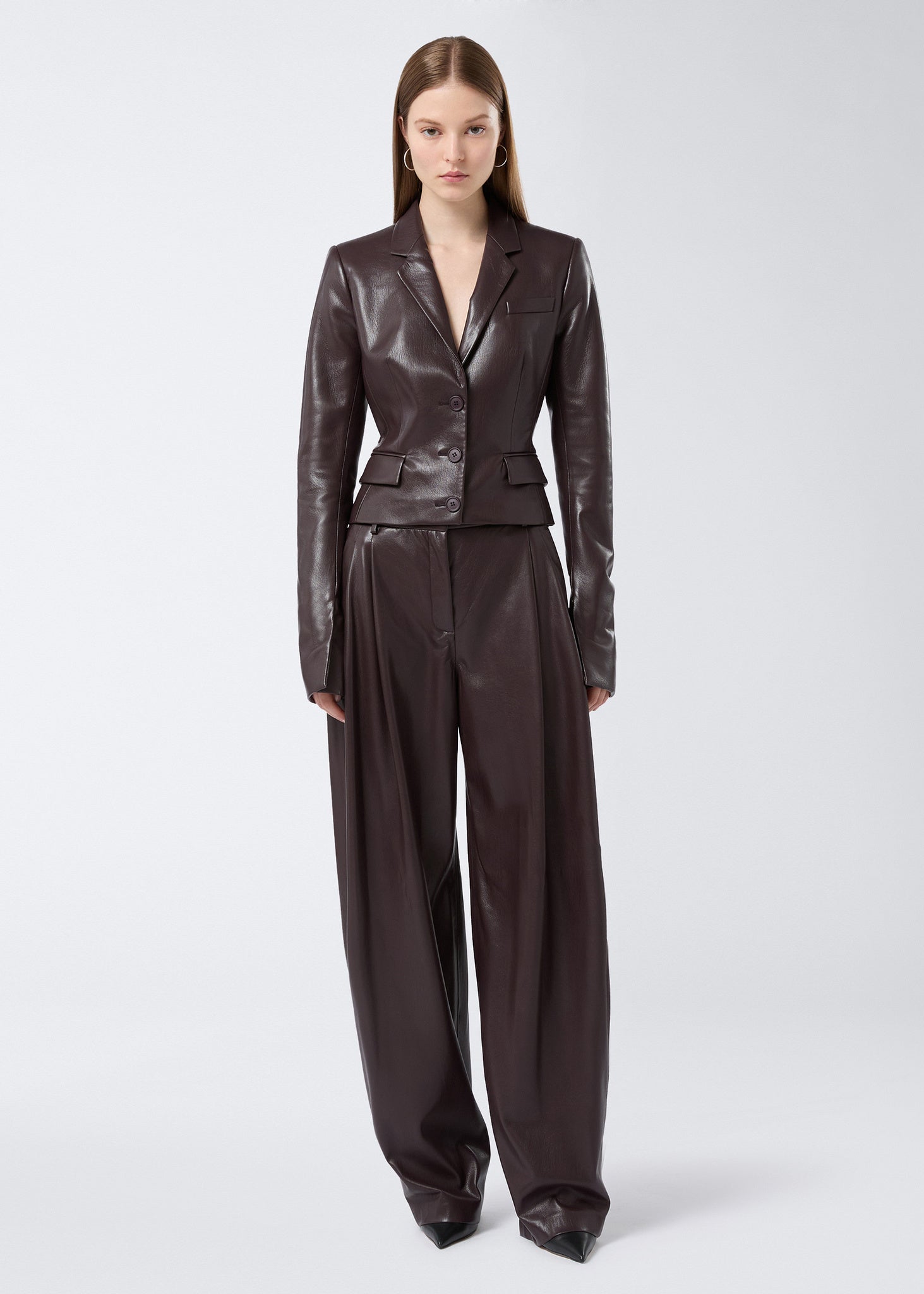 Frontal view of woman wearing Zefira Blazer in cabernet vegan leather with a fitted, cropped silhouette, notched lapel, three-button closure, and waist pockets.