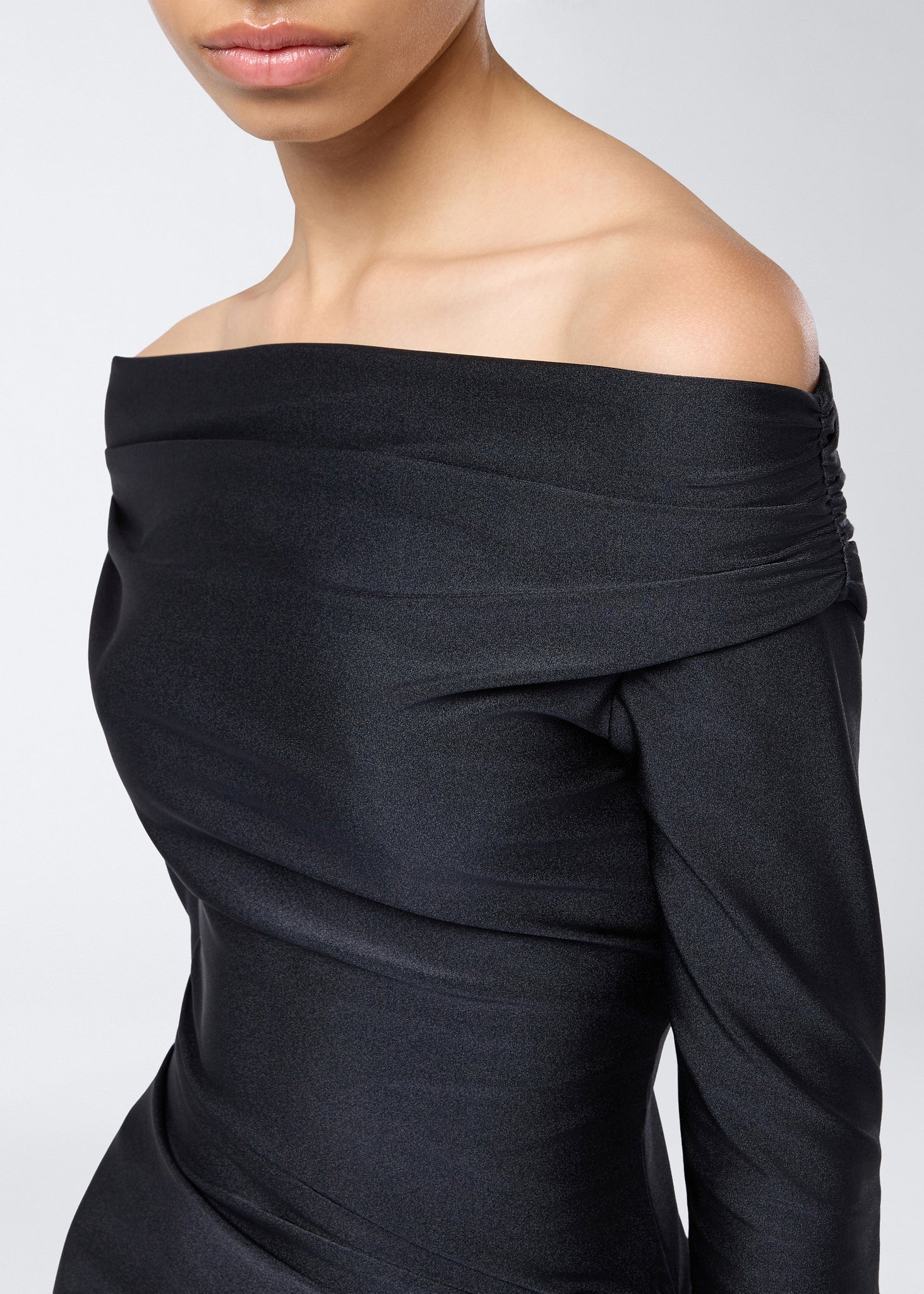 Detail view of the Wallis Jumpsuit showing the off-the-shoulder neckline and ruched black shiny lycra fabric with sculpted draping at the waist.