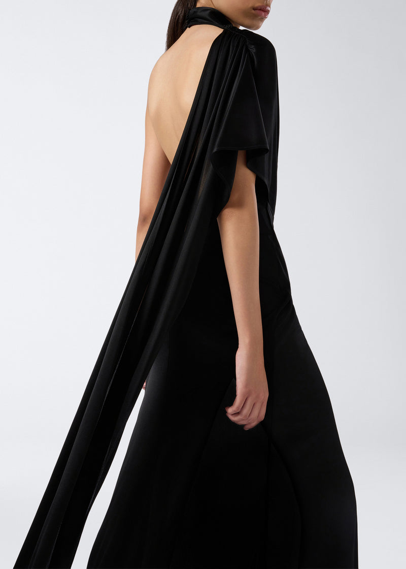 
                          Side view of a woman wearing the Waverly Maxi Dress in black shiny jersey, featuring a dramatic cape effect draping from the shoulder and a high slit.
                        