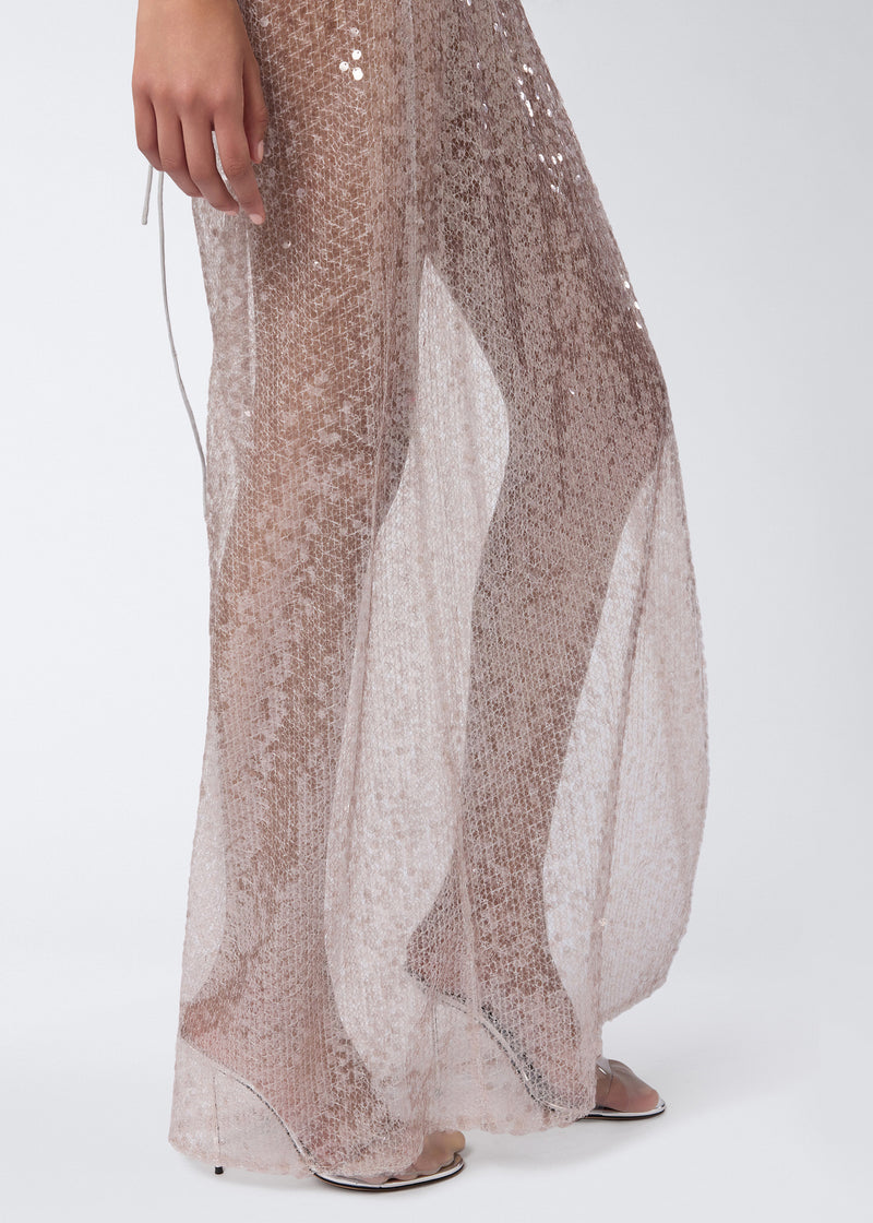 
                          Detail view of the West Maxi Dress showing steel-colored sequin fabric, sheer texture, and part of a hand and foot in high-heeled sandals.
                        