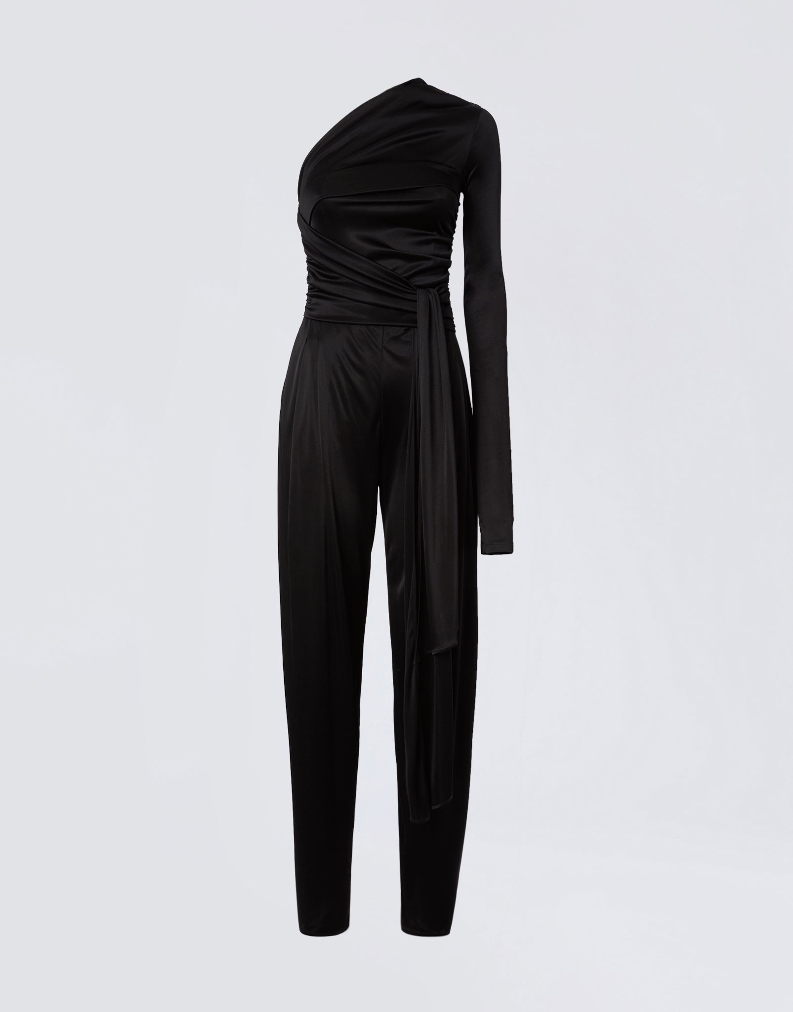 Frontal view of the Webster Jumpsuit, a black shiny jersey women’s piece with one-shoulder, one long sleeve, a waist-wrapping belt, and straight-leg pants.