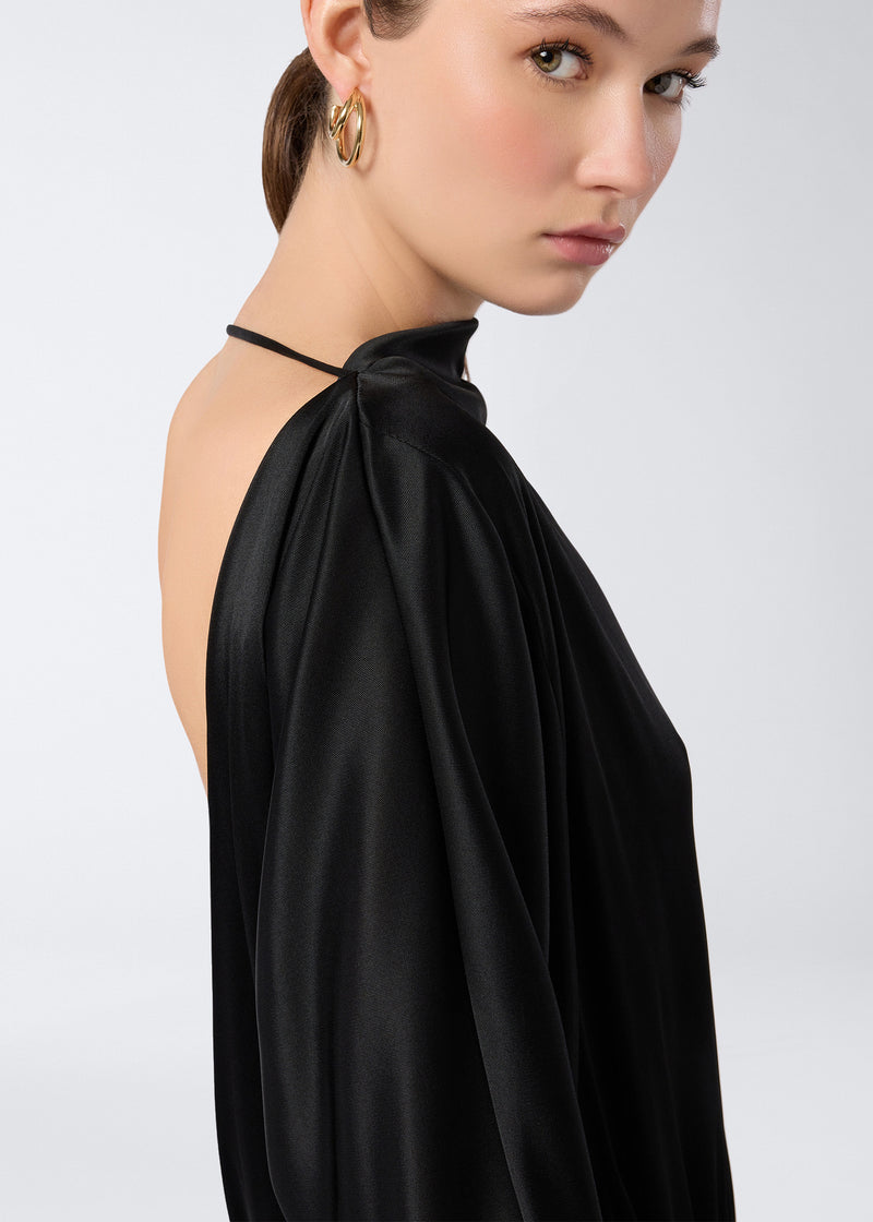 
                          Side view shows model wearing Winnie Playsuit in black shiny jersey with an open back, single neck band, and long sleeves, highlighting soft curved lines.
                        