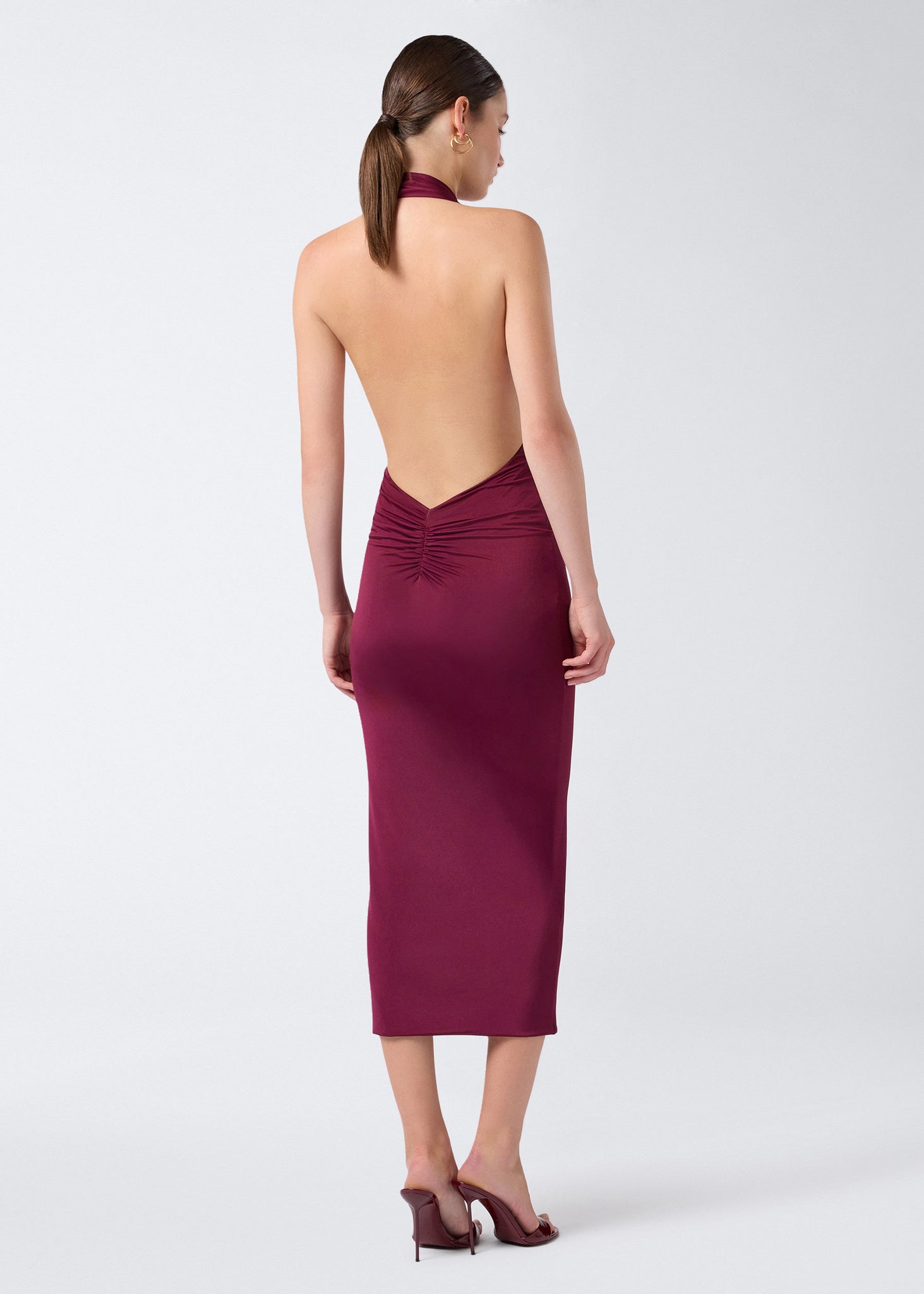 Rear view of a woman wearing the Zendaya Midi Dress in cabernet lightweight jersey, showcasing an open back, halterneck strap, and ruched waist detail.