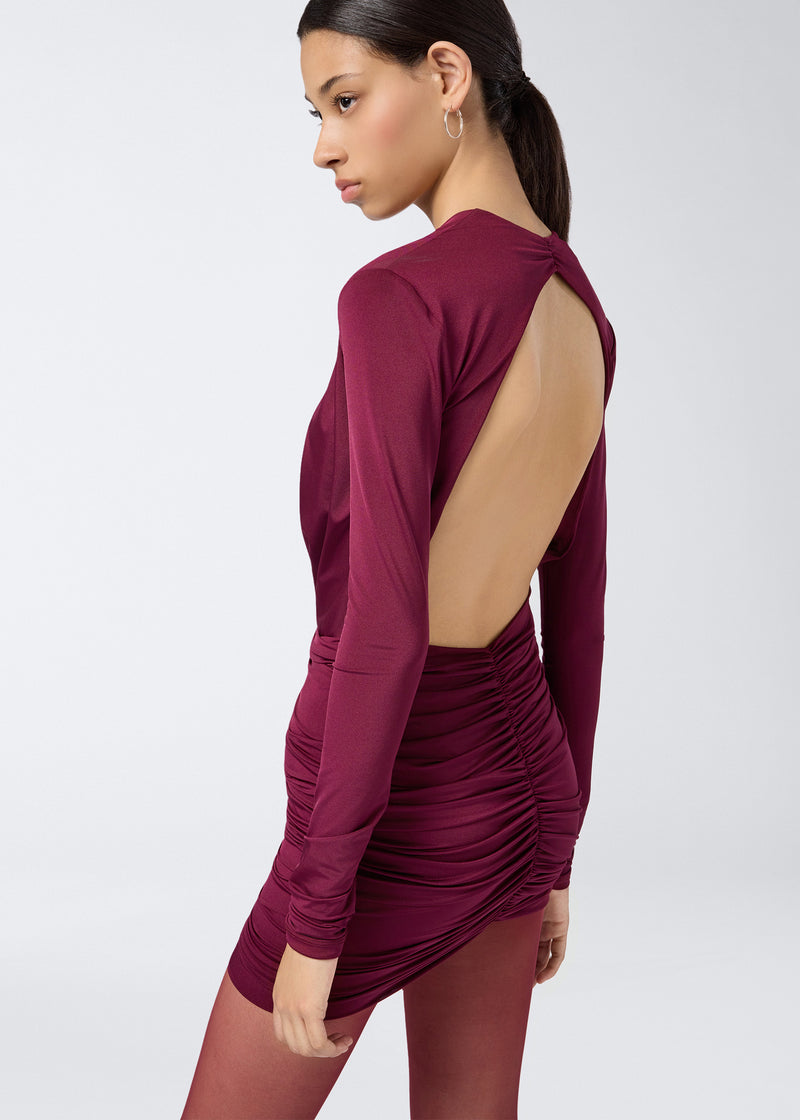 
                          Side view of a woman wearing the Zelda Mini Dress in cabernet lightweight jersey, showing an open back and all-over ruched detail on the skirt.
                        