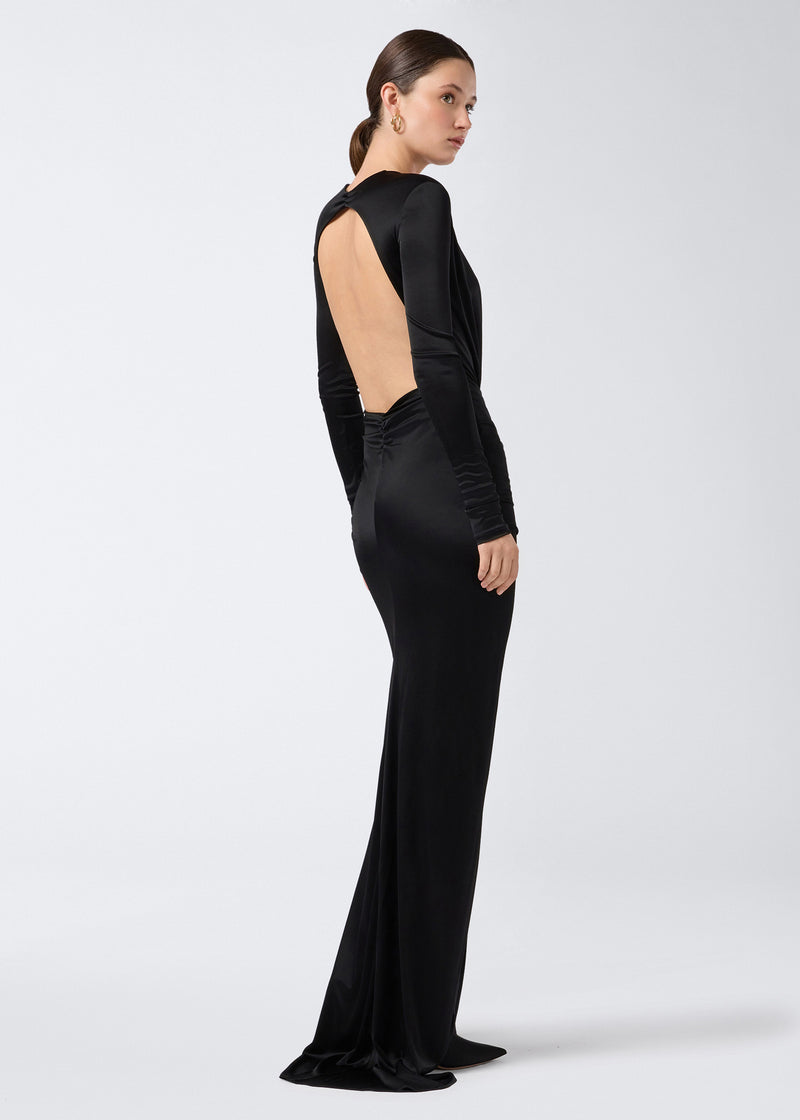 
                          Side view of a woman wearing the Zelda Maxi Dress, a long black shiny jersey dress with long sleeves, a plunging open back, and a floor-length skirt.
                        