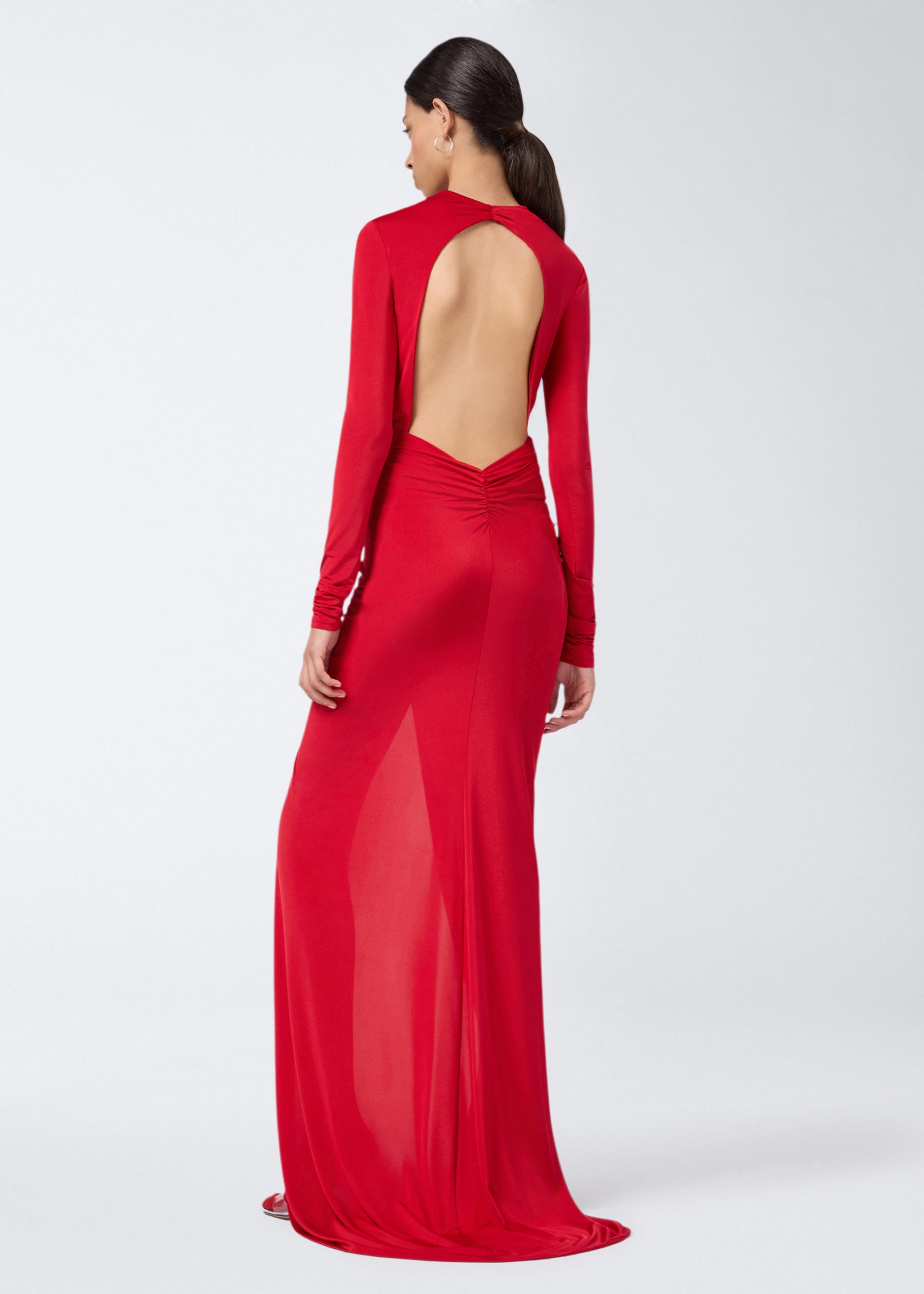Rear view shows model wearing the Zelda Maxi Dress in red lightweight jersey, featuring an open back, long sleeves, and ruched detailing on the skirt.